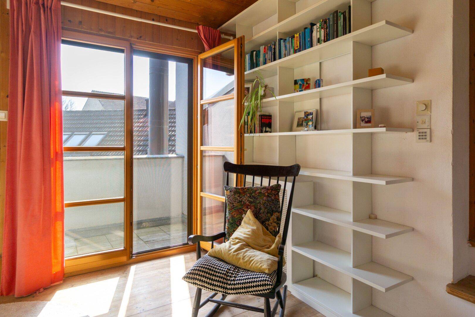 Schlafzimmer mit Zugang zu einem kleinen Balkon, Holzbalkendecke und Bücherregal.
