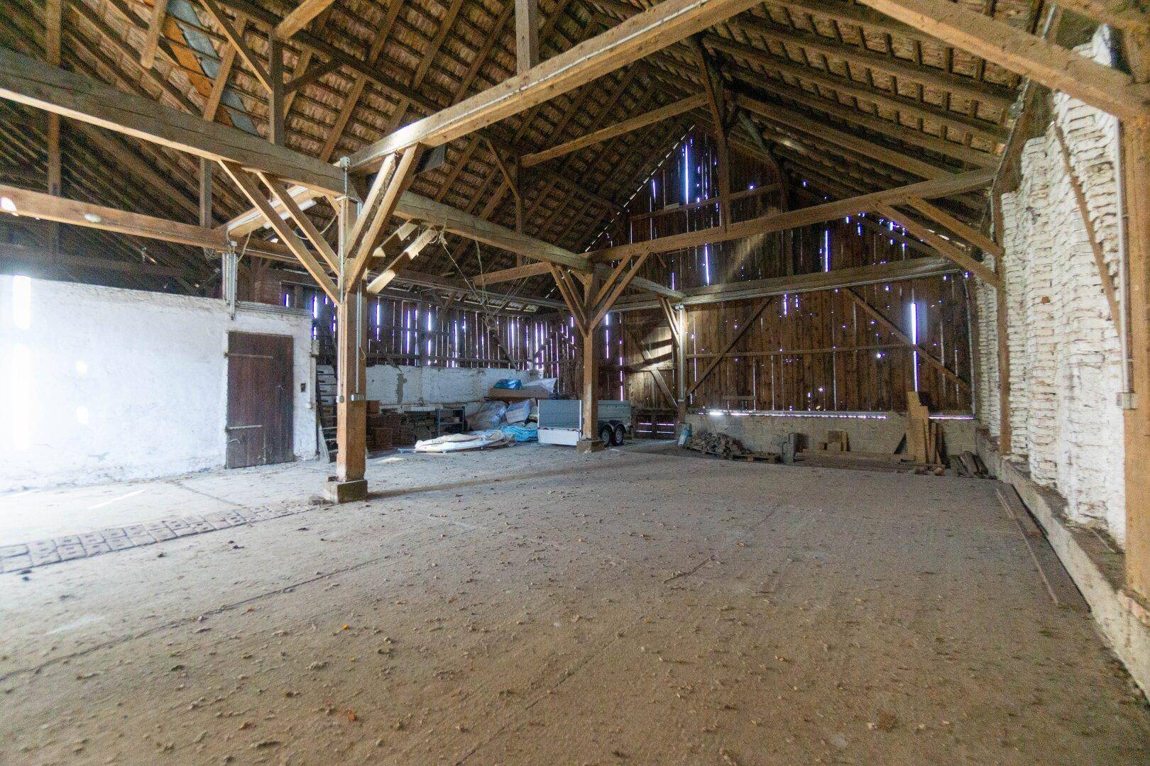 Geräumiger Innenraum einer Scheune mit Holzbalkenkonstruktion und viel Platz.