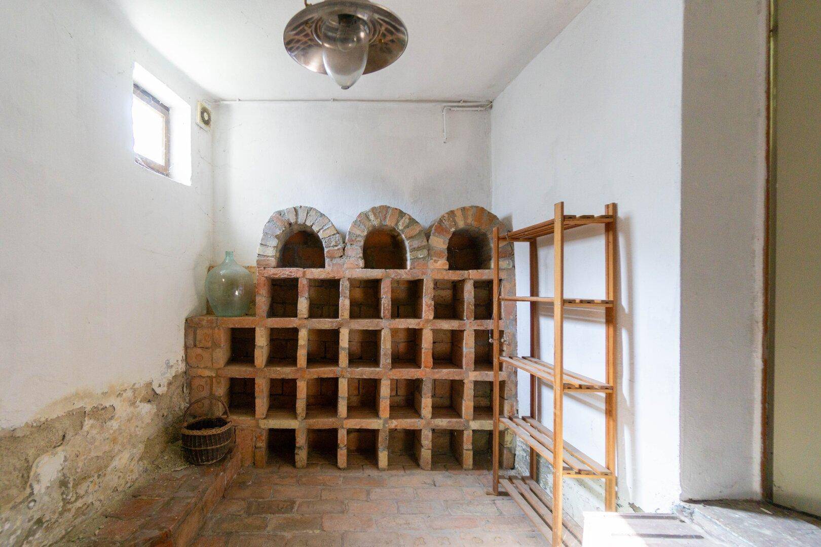 Rustikaler Weinkeller mit gemauerten Nischen für Flaschen und Holzregalen.