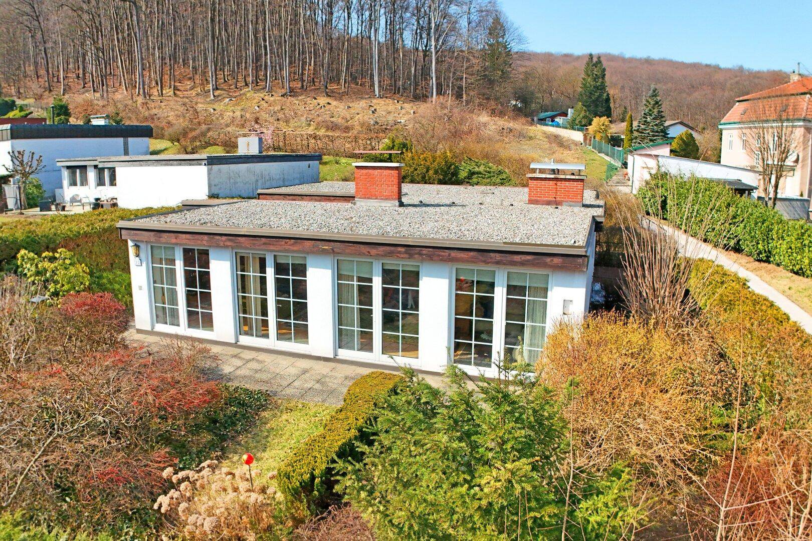 Ansicht des Hauses von oben mit Flachdach und zwei Schornsteinen, eingebettet in die grüne Umgebung.