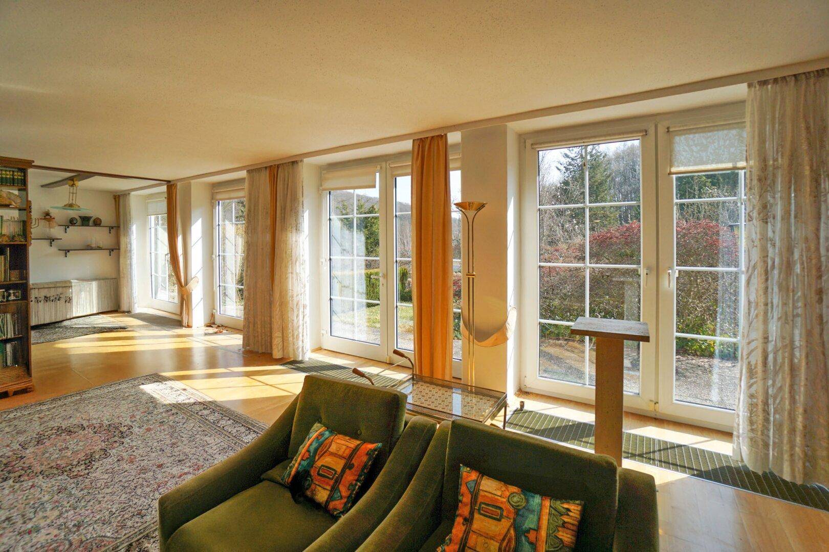 Helles Wohnzimmer mit großen Fenstern, die viel Tageslicht hereinlassen und Blick ins Grüne bieten.