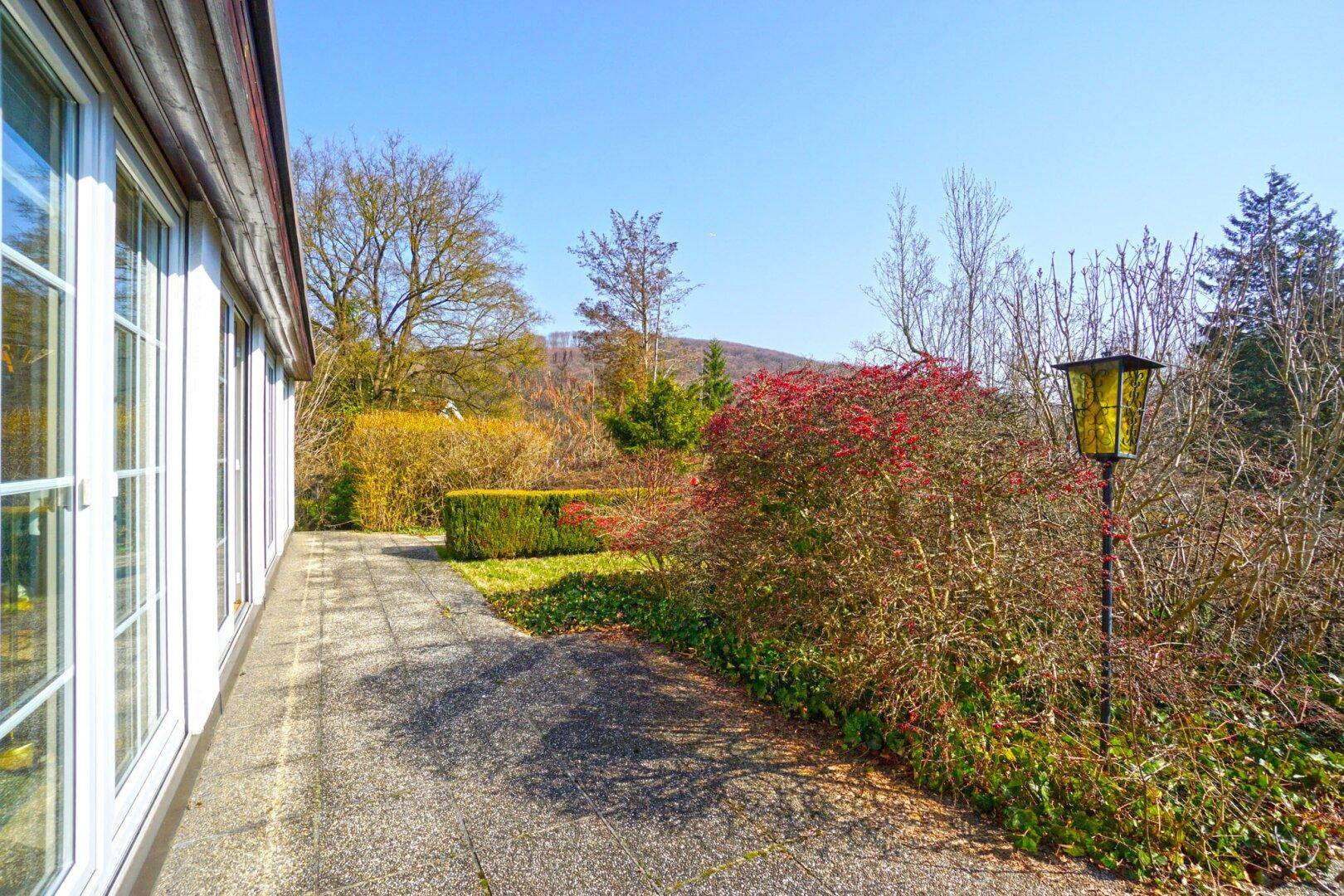 Gepflasterte Terrasse entlang des Hauses mit Blick auf den Garten und die umliegende Natur.