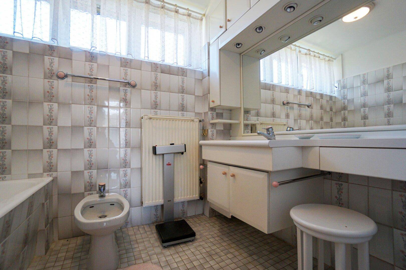 Badezimmer mit Fliesen an Wänden und Boden, ausgestattet mit Badewanne, Bidet und Doppelwaschbecken.