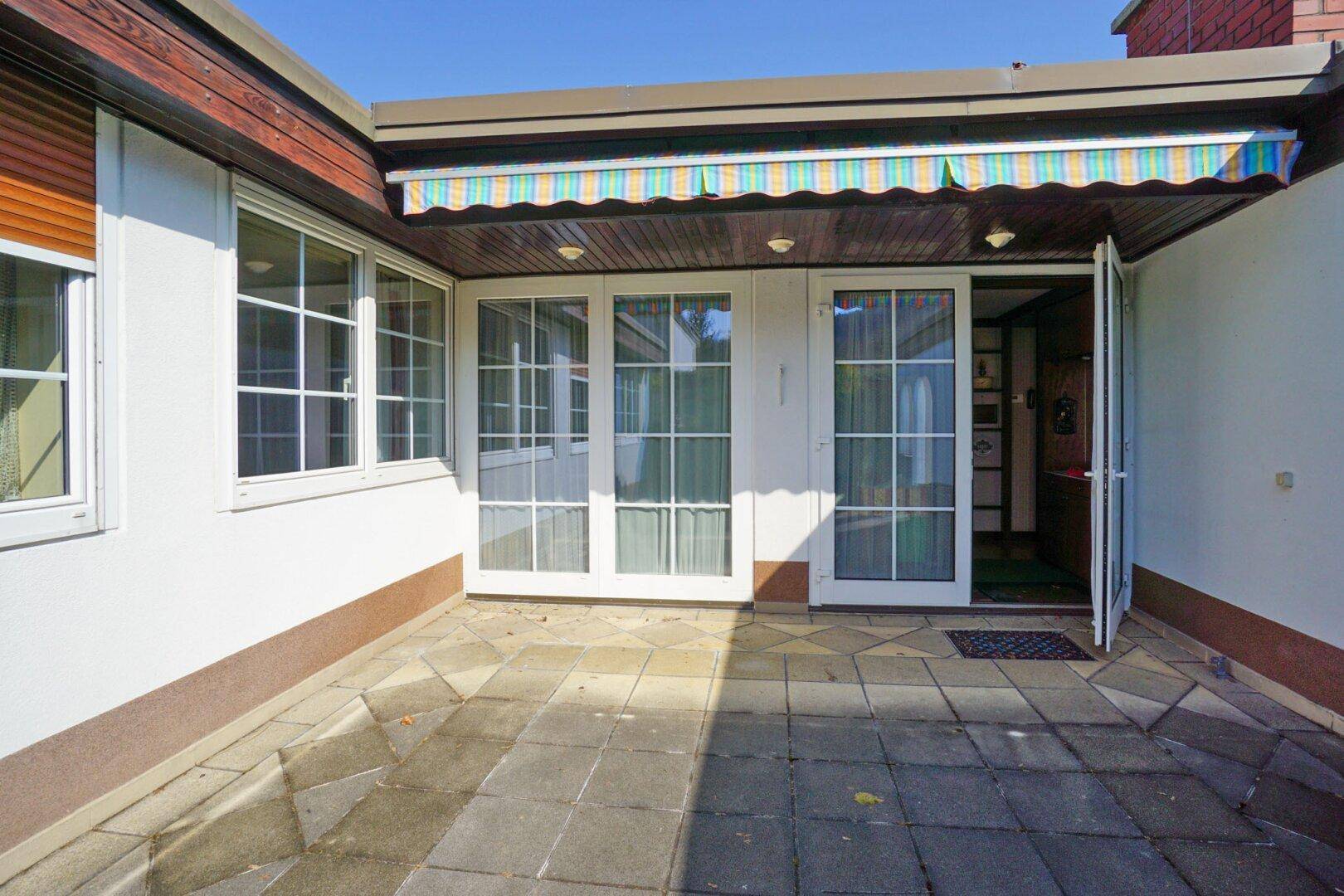 Gepflasterte Terrasse mit Markise und Zugang zum Haus, ideal für entspannte Stunden im Freien.