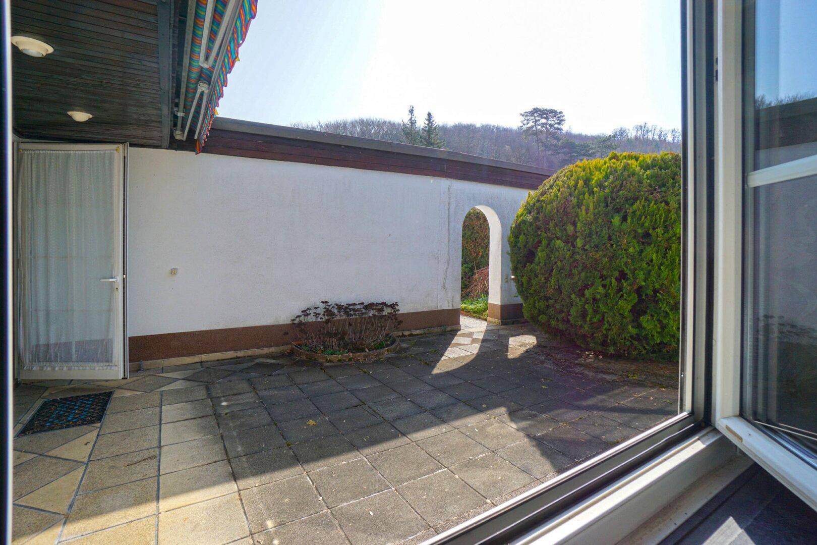 Sonnige Innenterrasse mit gepflastertem Boden und einem dekorativen Torbogen, umgeben von einer Mauer.