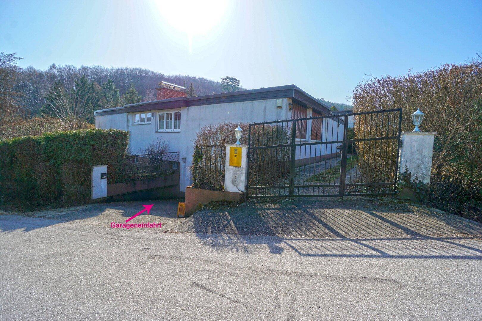 Einfahrt zum Grundstück mit Garageneinfahrt und einem schmiedeeisernen Tor, umgeben von Hecken.