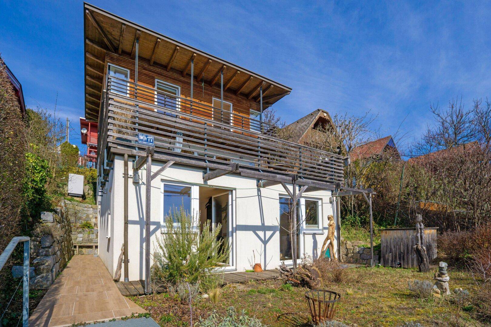 Seitenansicht des Hauses mit Holzverkleidung und Balkonen, umgeben von natürlicher Vegetation.