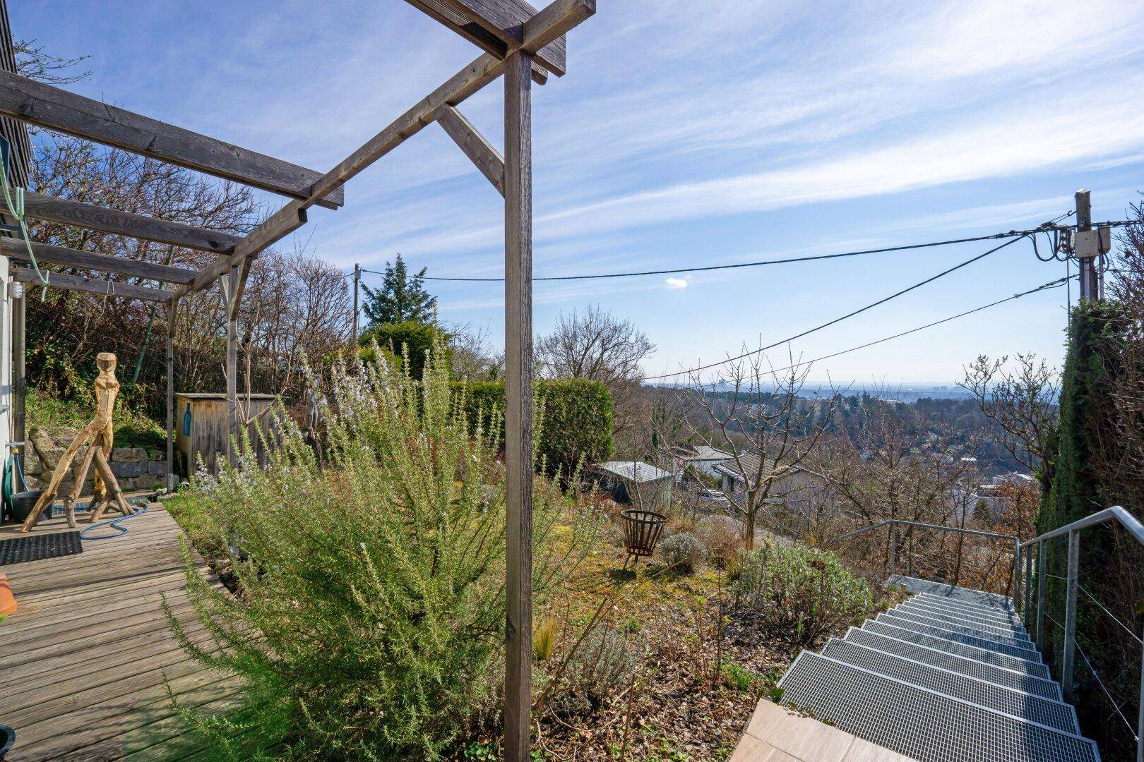 Gartenbereich mit Holzdeck, Treppe und Pergola, bietet einen weiten Blick ins Grüne.