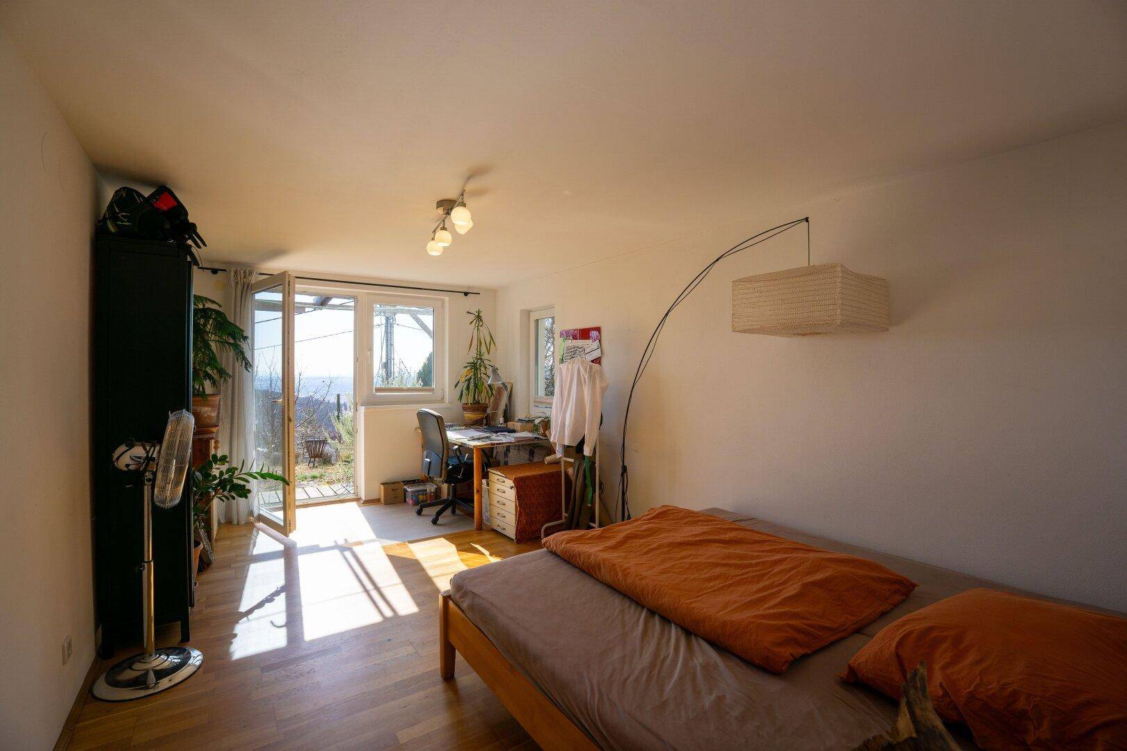 Gemütliches Schlafzimmer mit Holzbett, Arbeitsbereich und großen Fenstern für viel Tageslicht.