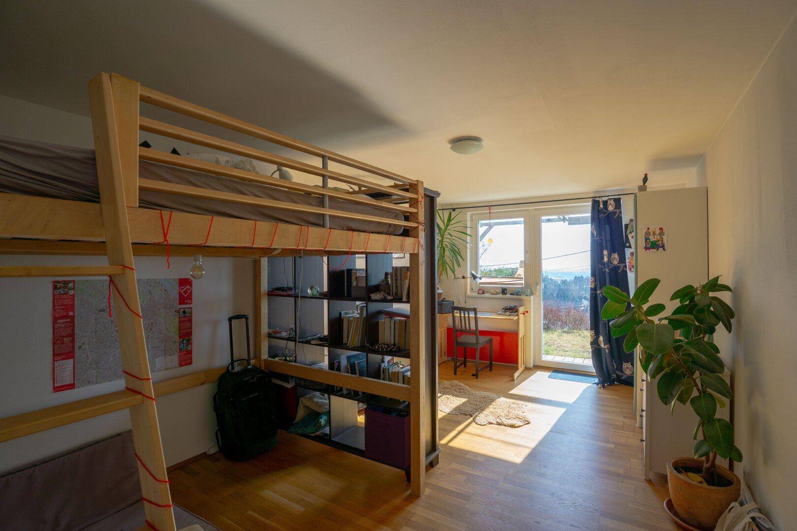 Helles Schlafzimmer mit Hochbett, Schreibtisch und Zugang zu einem Balkon mit schöner Aussicht.