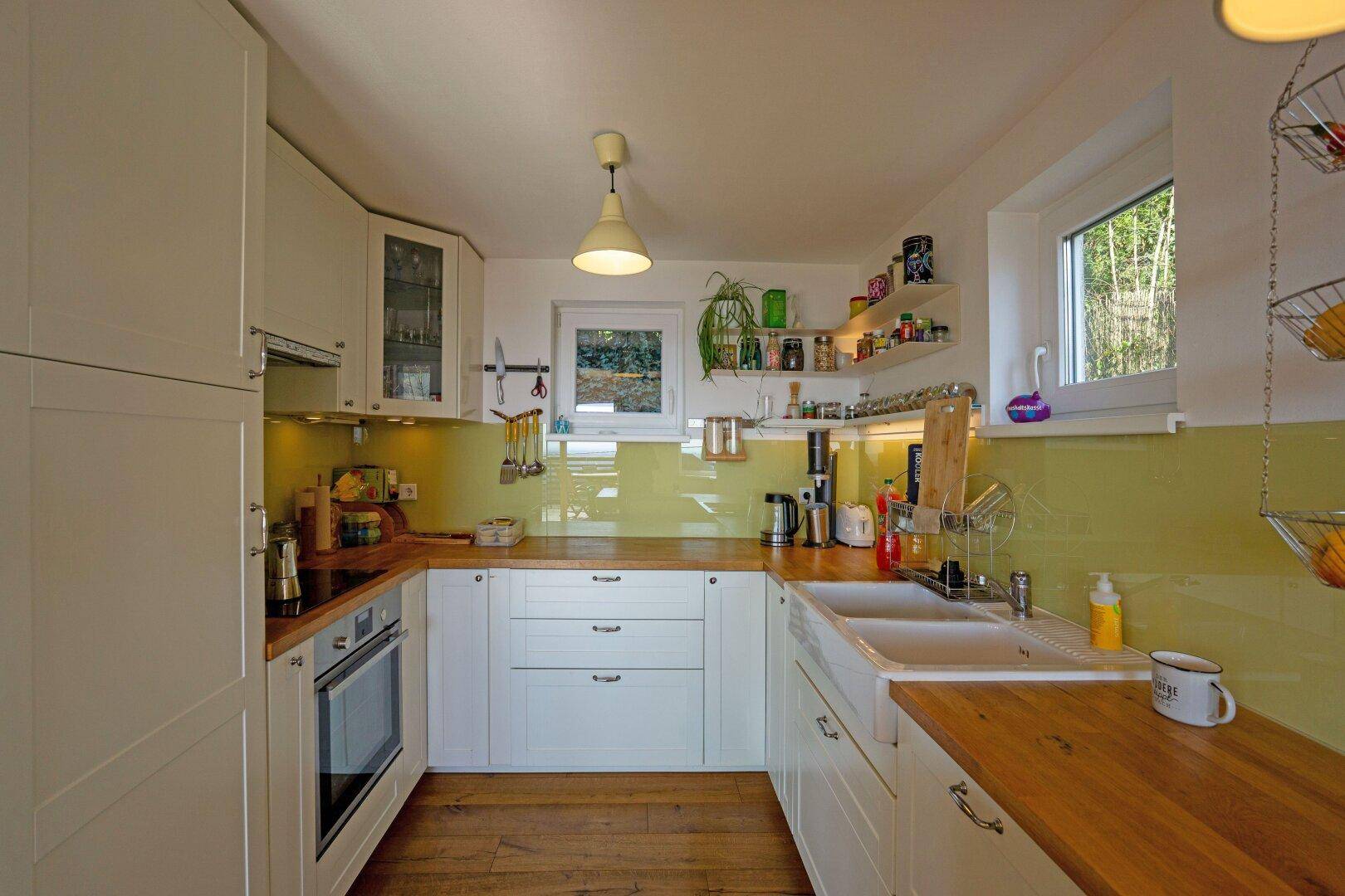 Helle Einbauküche mit weißen Schränken, Holz-Arbeitsplatten und einer modernen grünen Rückwand.