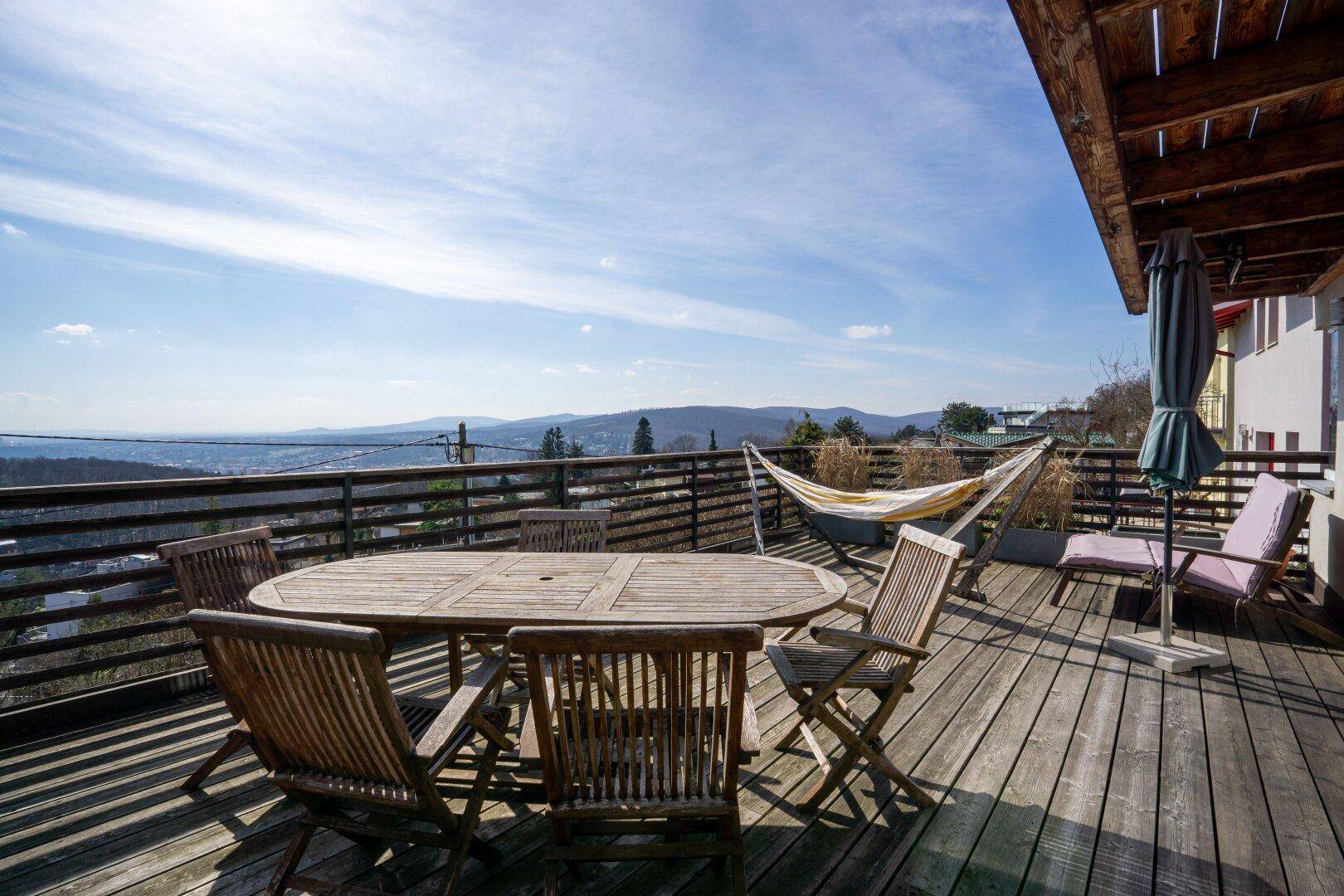 Große Holzterrasse mit Esstisch, Hängematte und weitem Blick über die hügelige Landschaft.