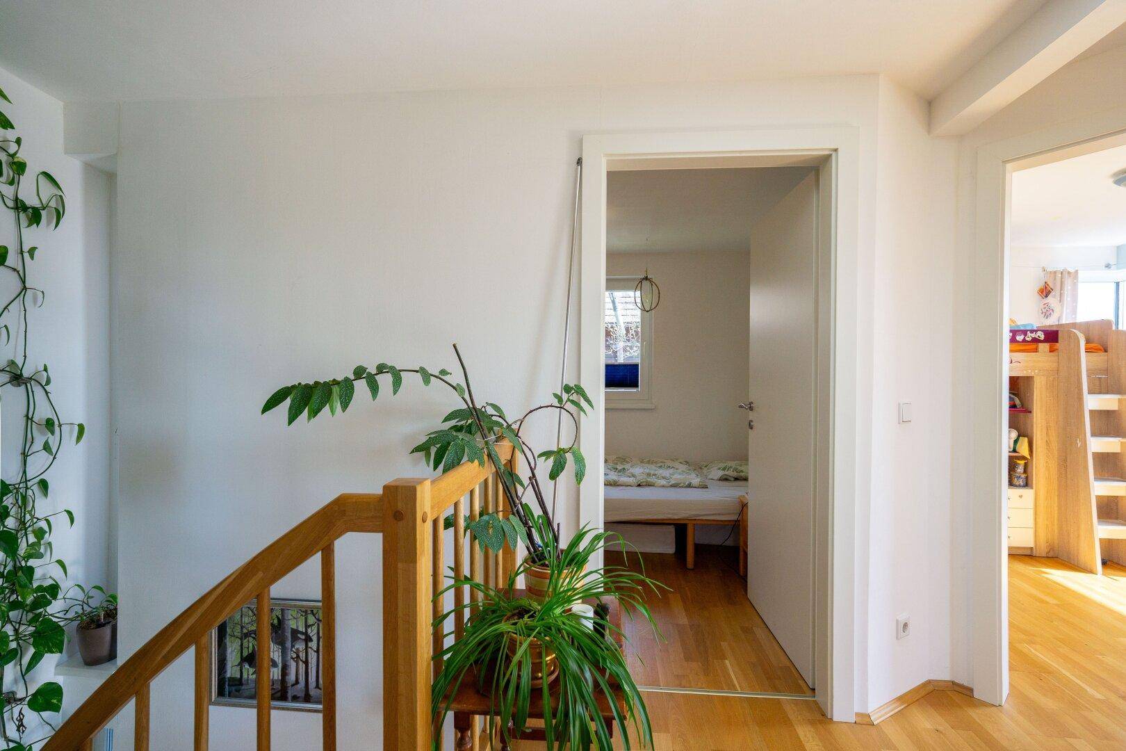 Heller Flur mit Holzboden und Blick in ein angrenzendes Schlafzimmer, das viel Tageslicht erhält.