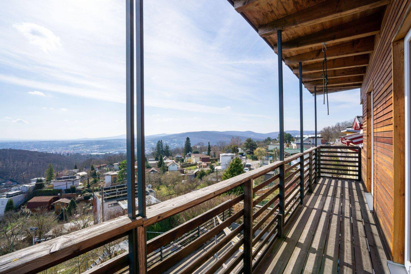 Langer Holzbalkon mit Geländer und weitem Blick über die hügelige Landschaft, ideal zum Entspannen.