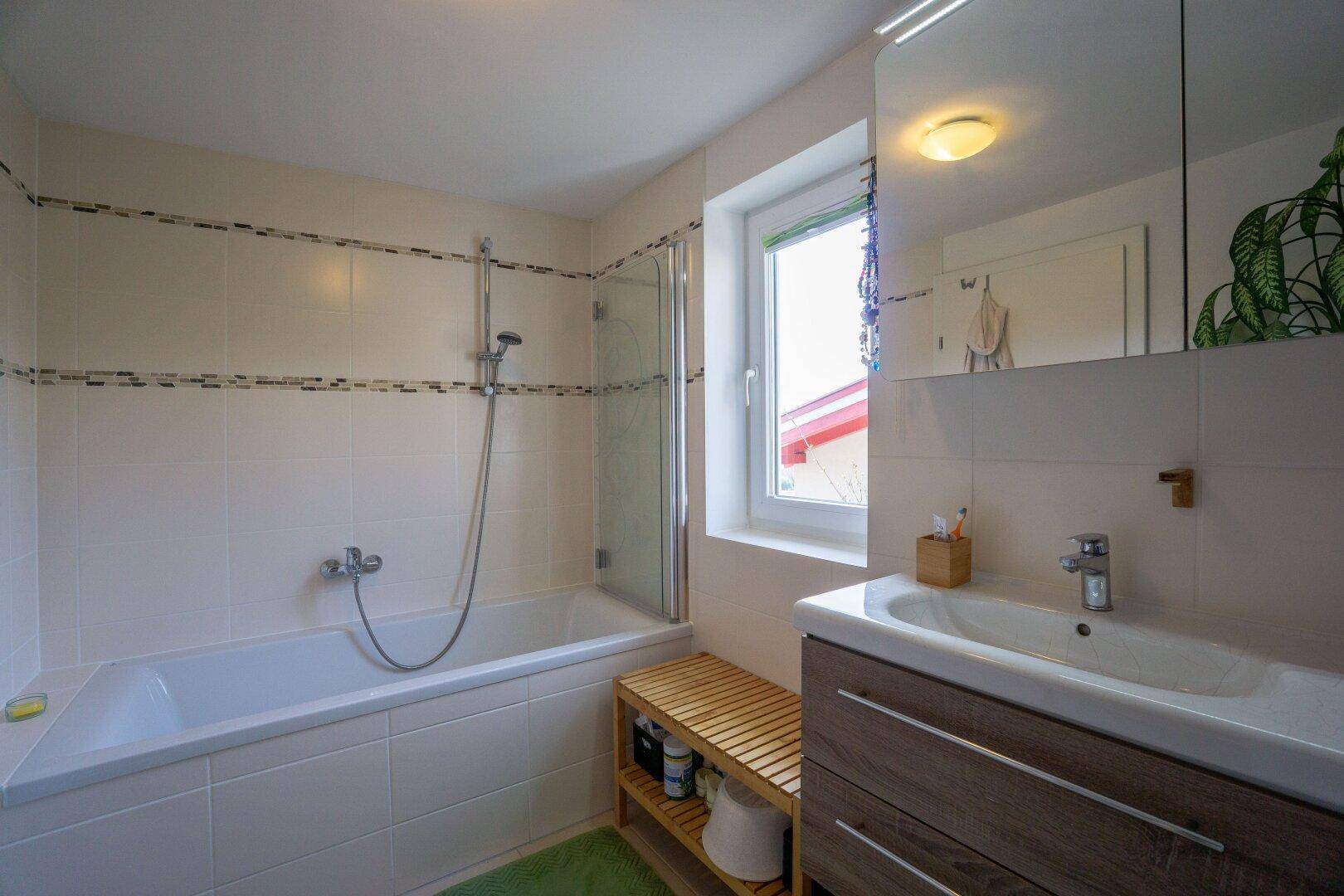 Helles Badezimmer mit Badewanne, Waschbecken und Spiegelschrank, gefliest in Weiß und Beige.