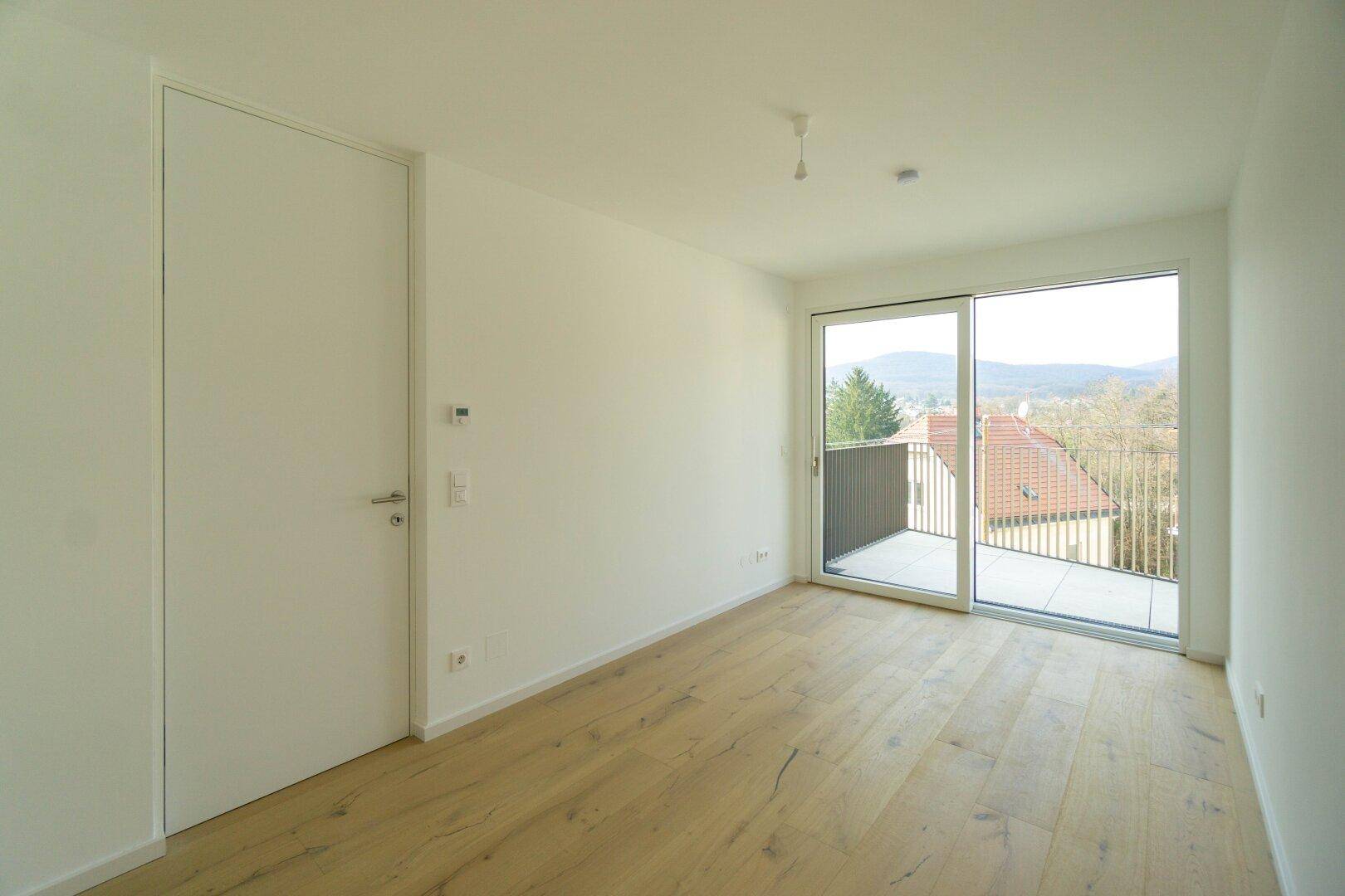 Helles Schlafzimmer mit Holzboden und großem Schiebefenster, das Zugang zu einem Balkon bietet.