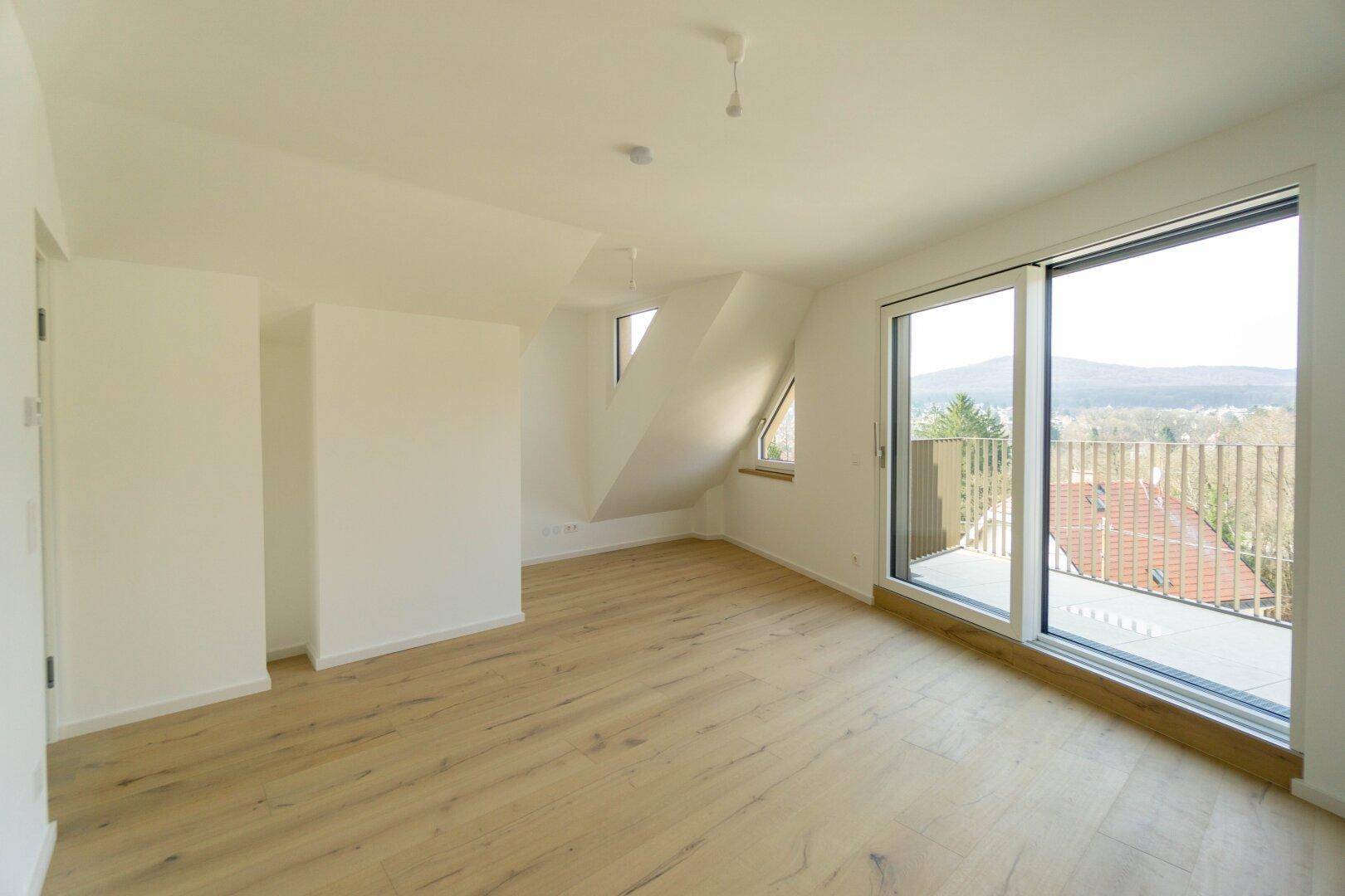 Geräumiges Dachgeschosszimmer mit Holzboden, schrägen Decken und Balkonzugang mit Weitblick.