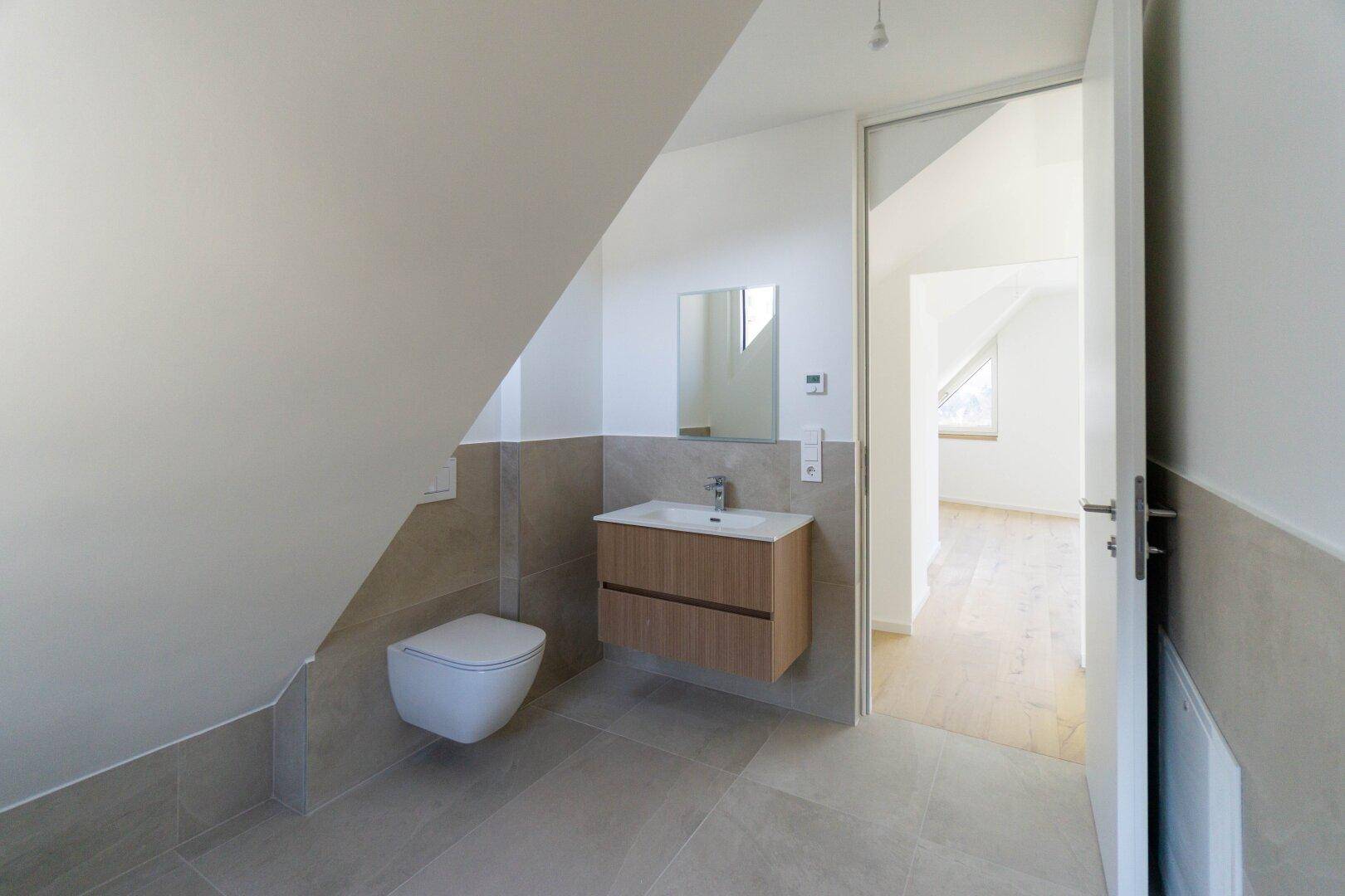Modernes Badezimmer im Dachgeschoss mit schräger Decke, beigefarbenen Fliesen und wandhängendem WC.