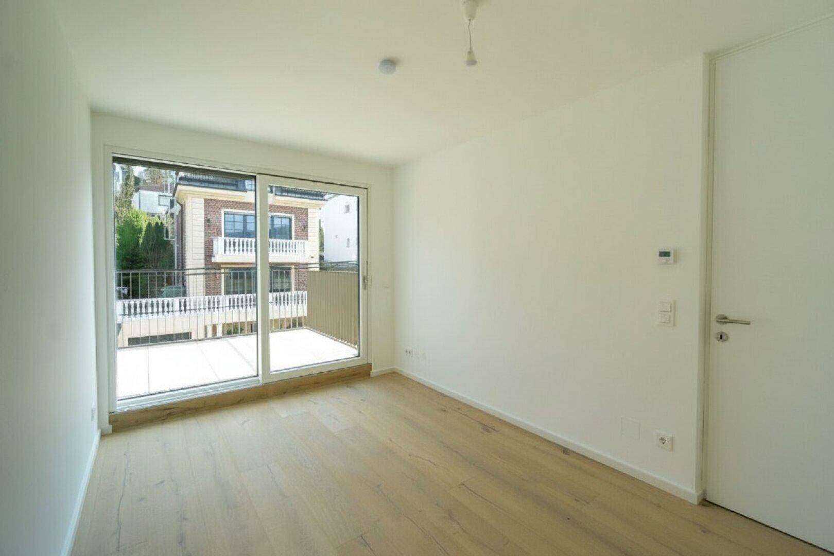 Helles Zimmer mit Holzboden und großem Schiebefenster, das Zugang zu einem Balkon bietet.