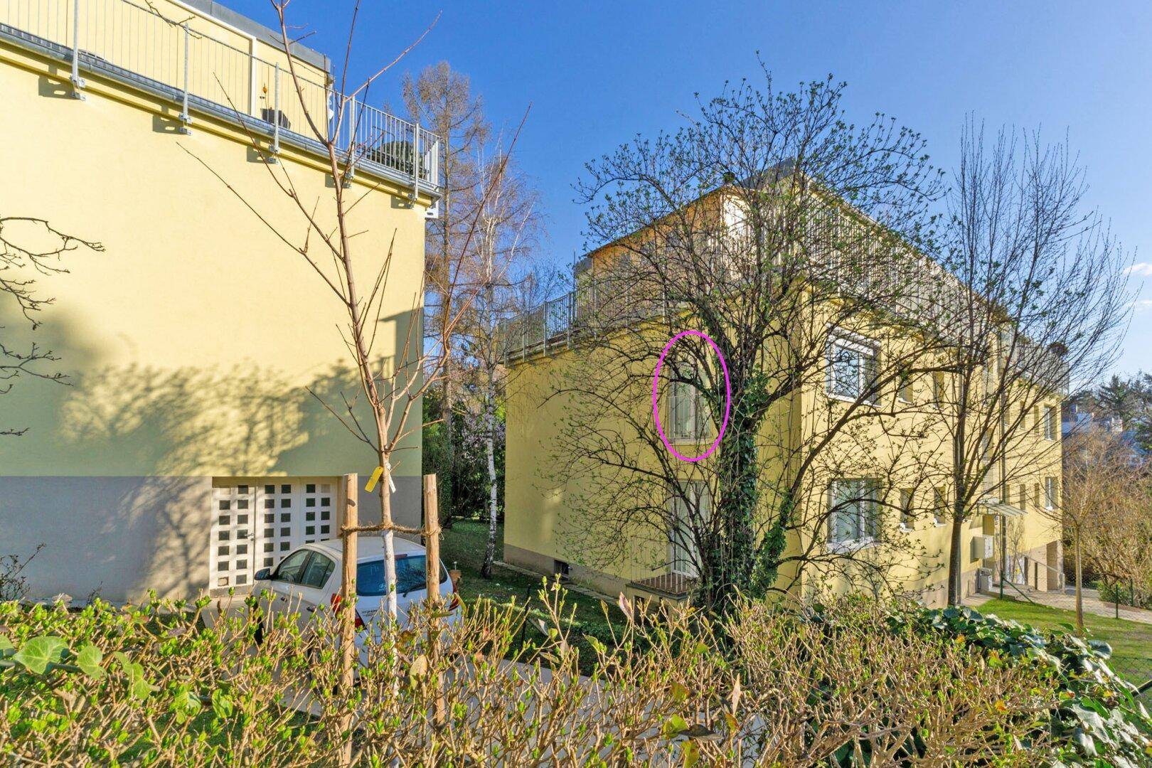 Seitenansicht des Gebäudes mit Bäumen und einem teilweise sichtbaren Carport.