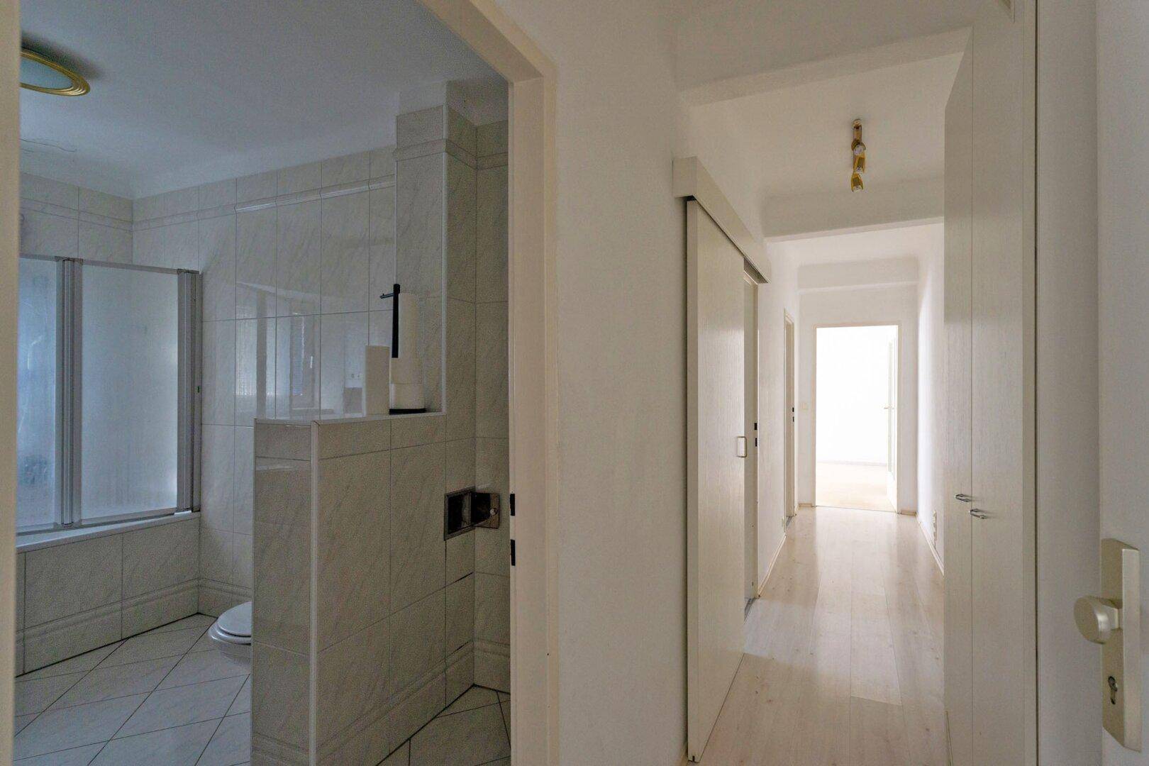 Heller Flur mit hellem Laminatboden und Blick in ein gefliestes Badezimmer.