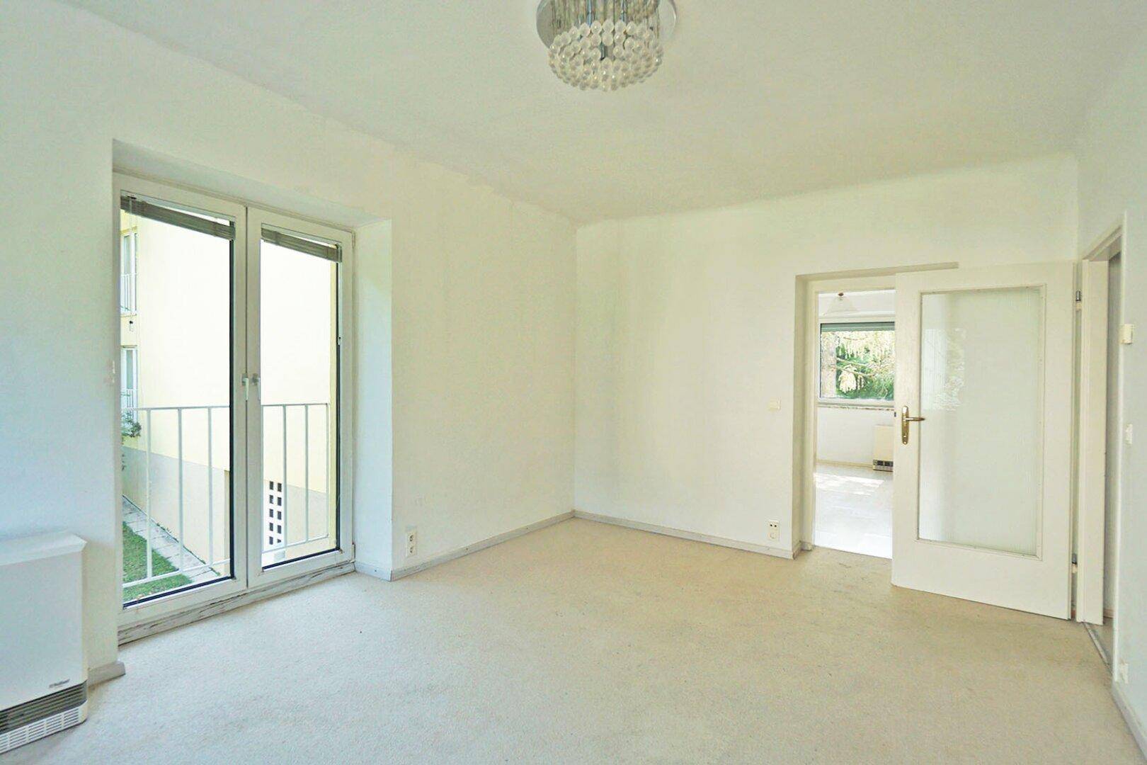 Leerer Raum mit Teppichboden, französischem Balkon und offener Tür zu einem weiteren Bereich.
