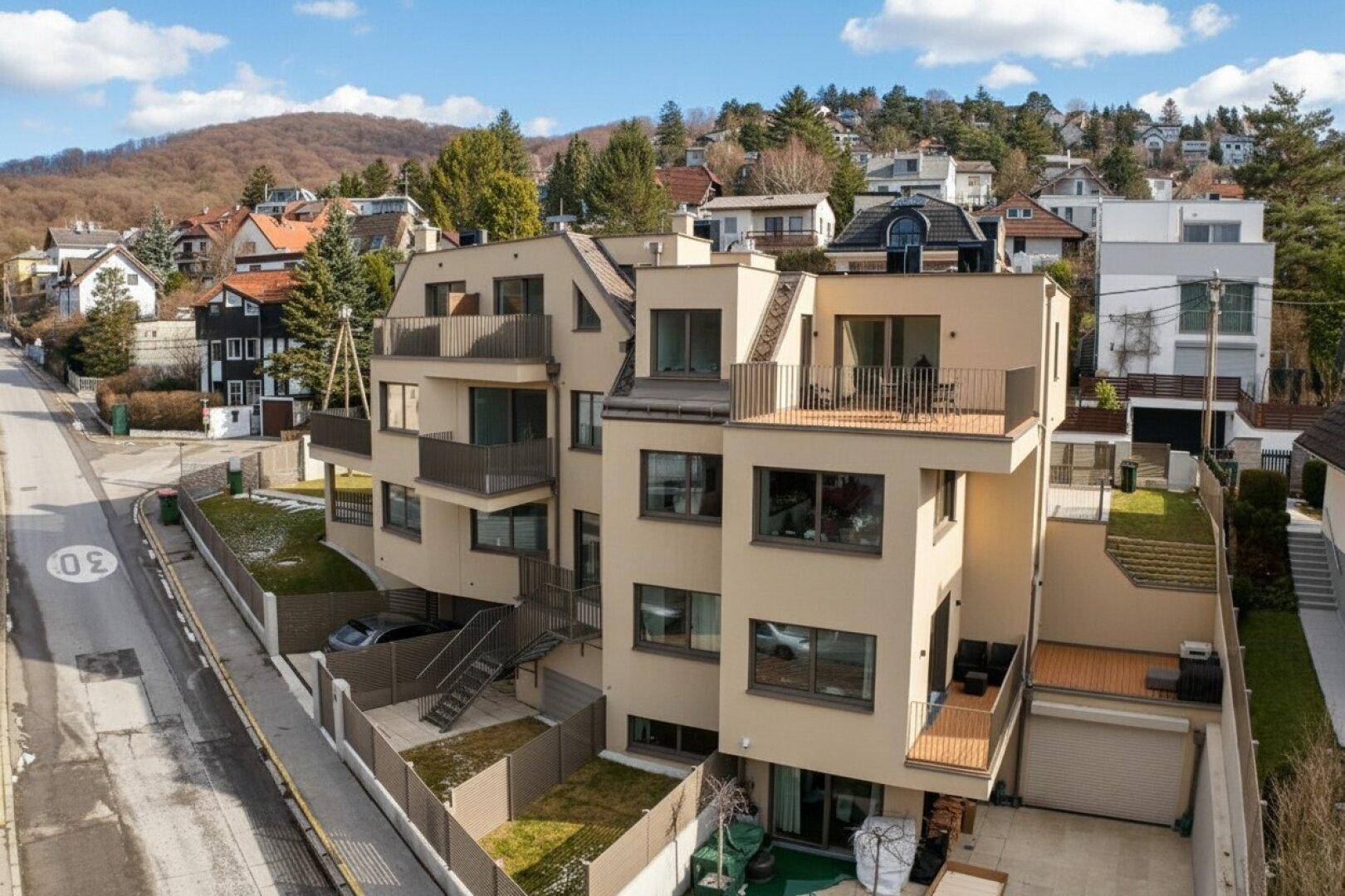 Moderne Wohnanlage mit mehreren Balkonen und Terrassen, eingebettet in eine grüne Hügellandschaft.
