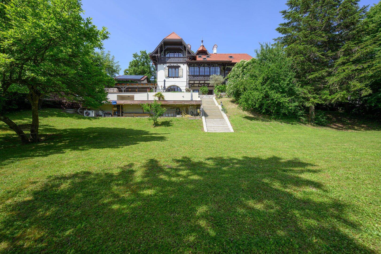 Weitläufiger grüner Garten mit Blick auf die elegante Villa und die umliegende Natur.