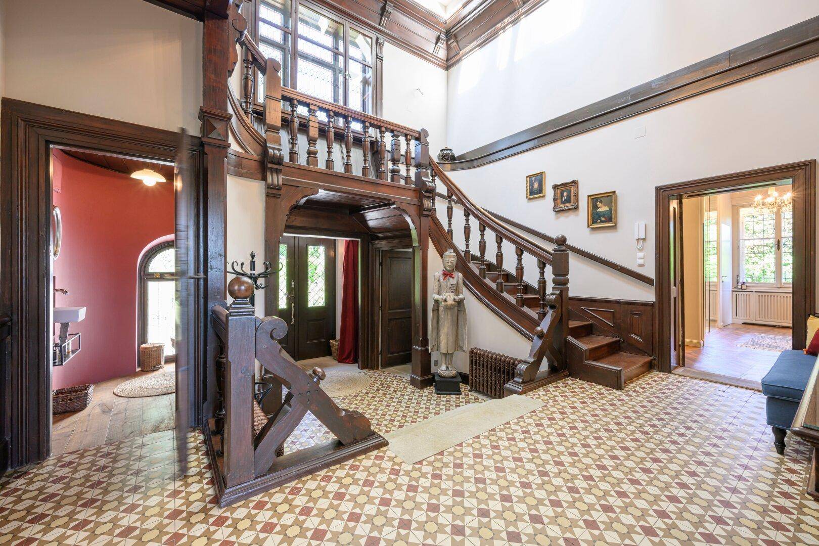 Beeindruckende Eingangshalle mit einer eleganten Holztreppe und gemusterten Fliesenböden.