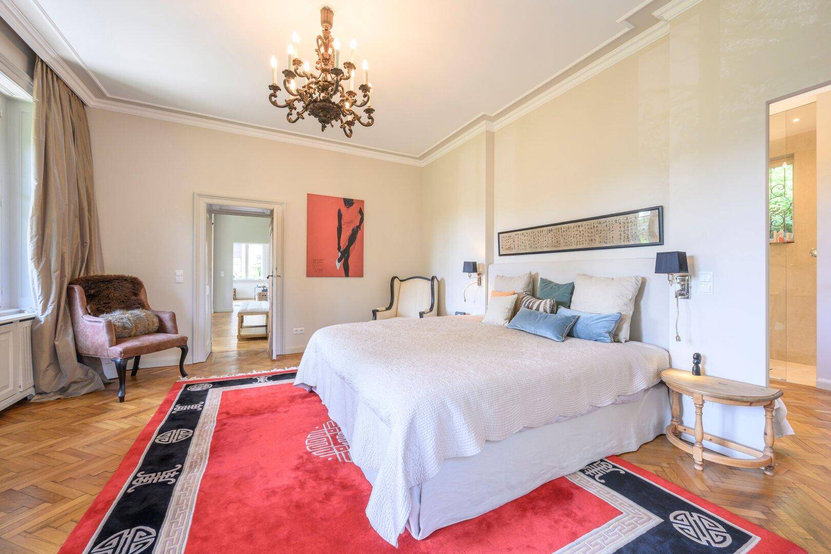 Elegantes Schlafzimmer mit Parkettboden, großem Bett und einem auffälligen roten Teppich.