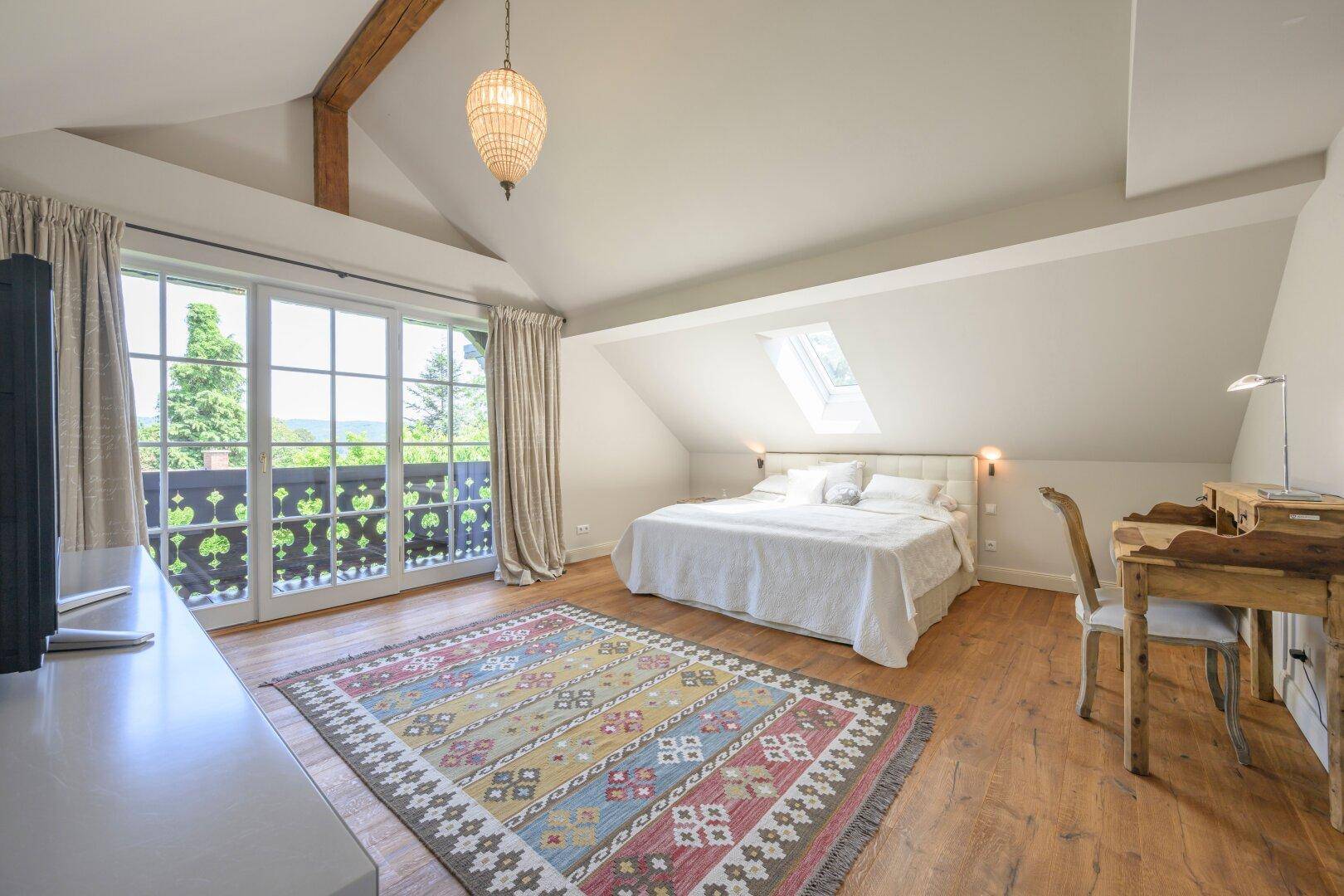 Geräumiges Schlafzimmer mit Balkonzugang, Dachfenster und einem Schreibtisch, bietet weite Ausblicke.