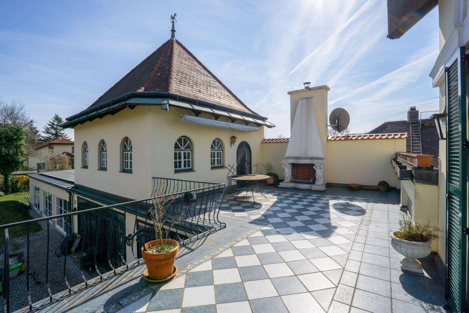 Große Dachterrasse mit Schachbrettmuster-Fliesen, Außenkamin und weitem Blick über die Dächer.
