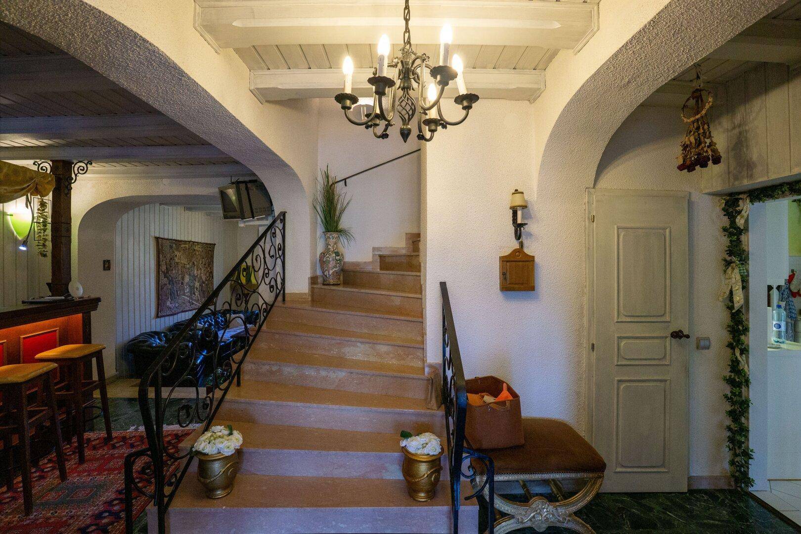Elegantes Treppenhaus mit schmiedeeisernem Geländer und Blick auf einen Barbereich im Untergeschoss.