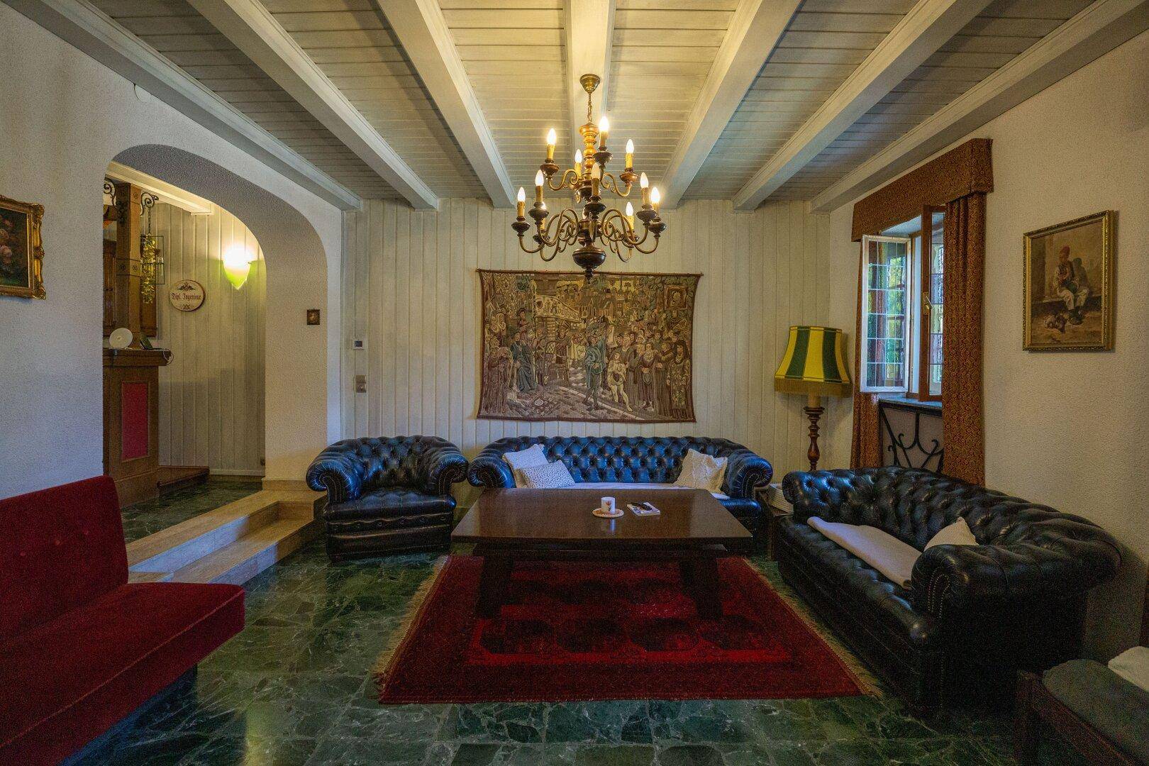 Klassisch eingerichtetes Wohnzimmer mit Chesterfield-Sofas, Holzbalkendecke und grünem Marmorboden.