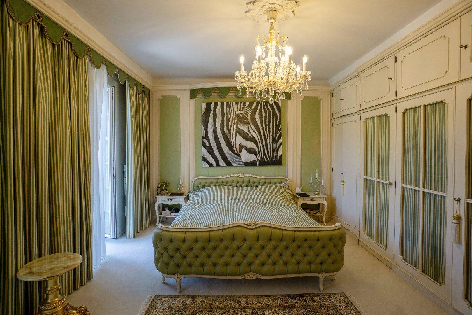 Elegantes Schlafzimmer mit grünem Polsterbett, Einbauschränken und einem Kronleuchter.