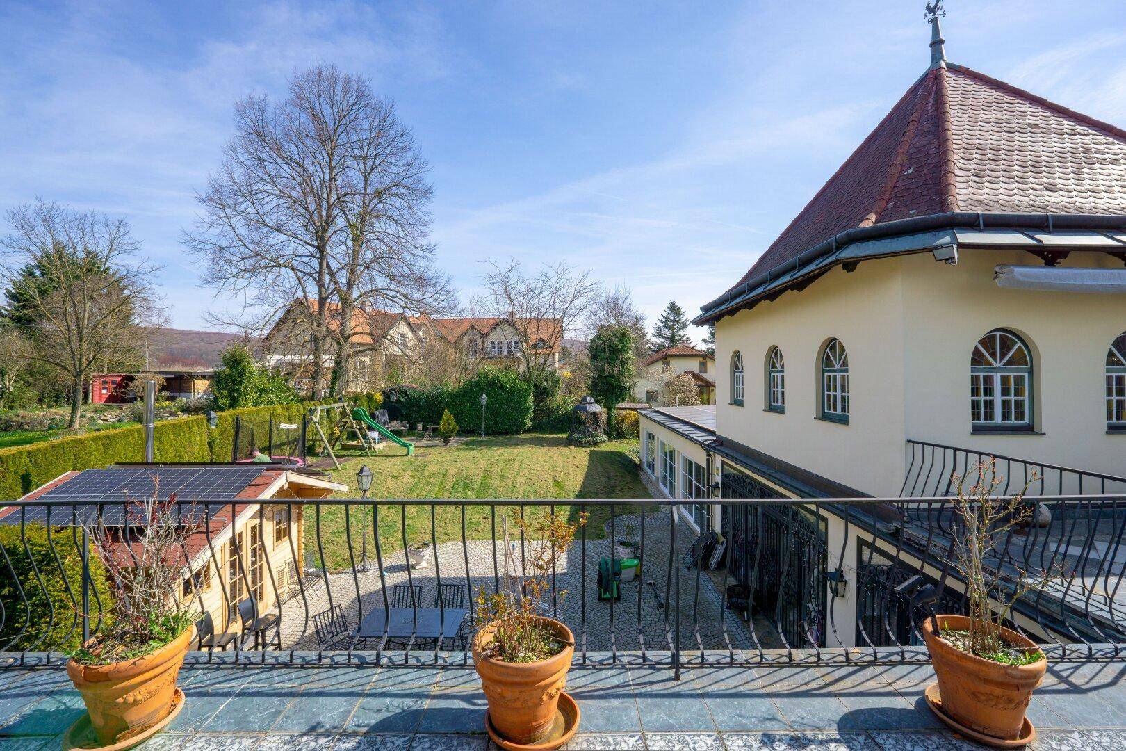Blick von der Terrasse auf den weitläufigen Garten mit Rasenfläche, Bäumen und Spielgeräten.