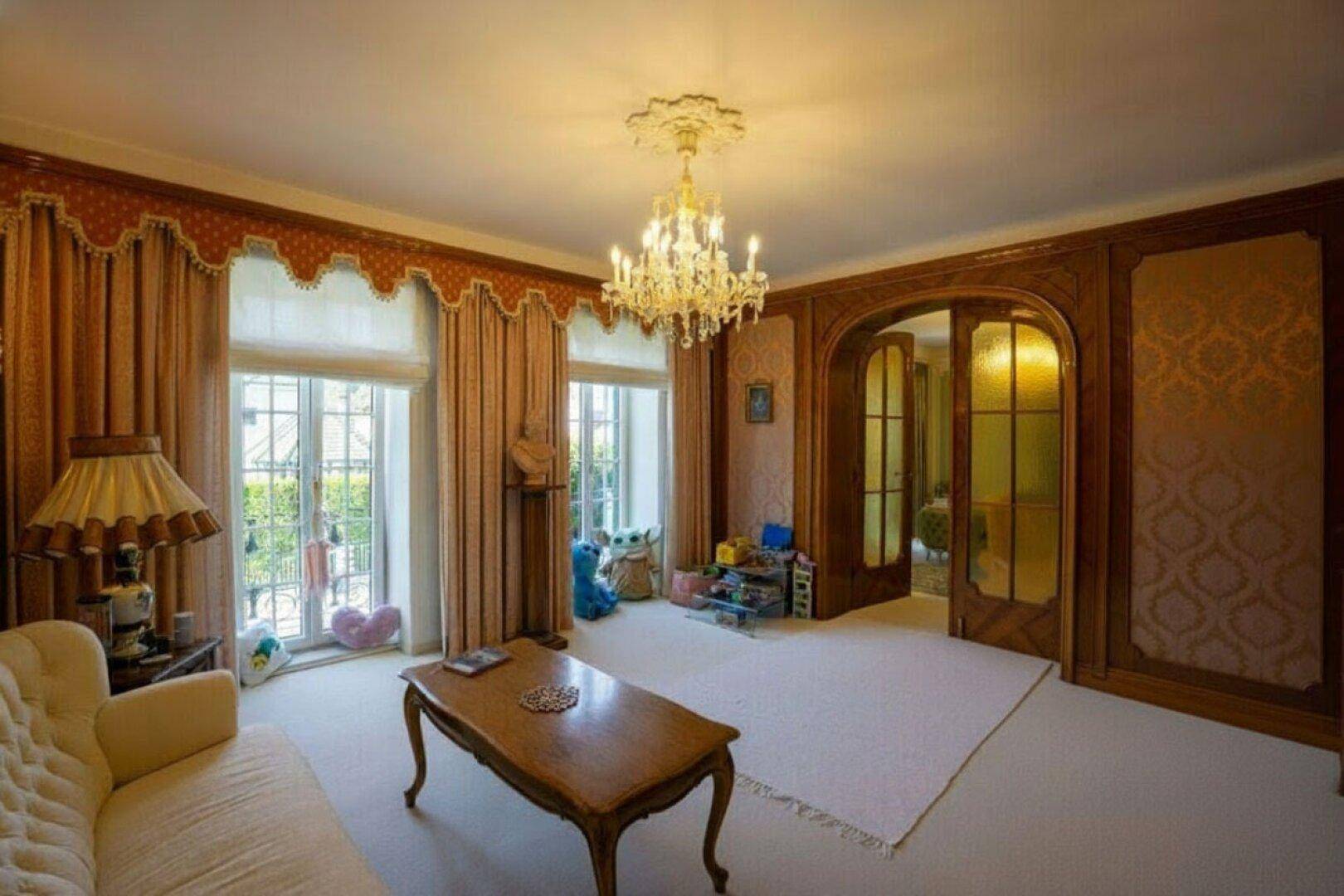 Gemütliches Wohnzimmer mit hellem Teppichboden, eleganten Vorhängen und einem Kronleuchter.