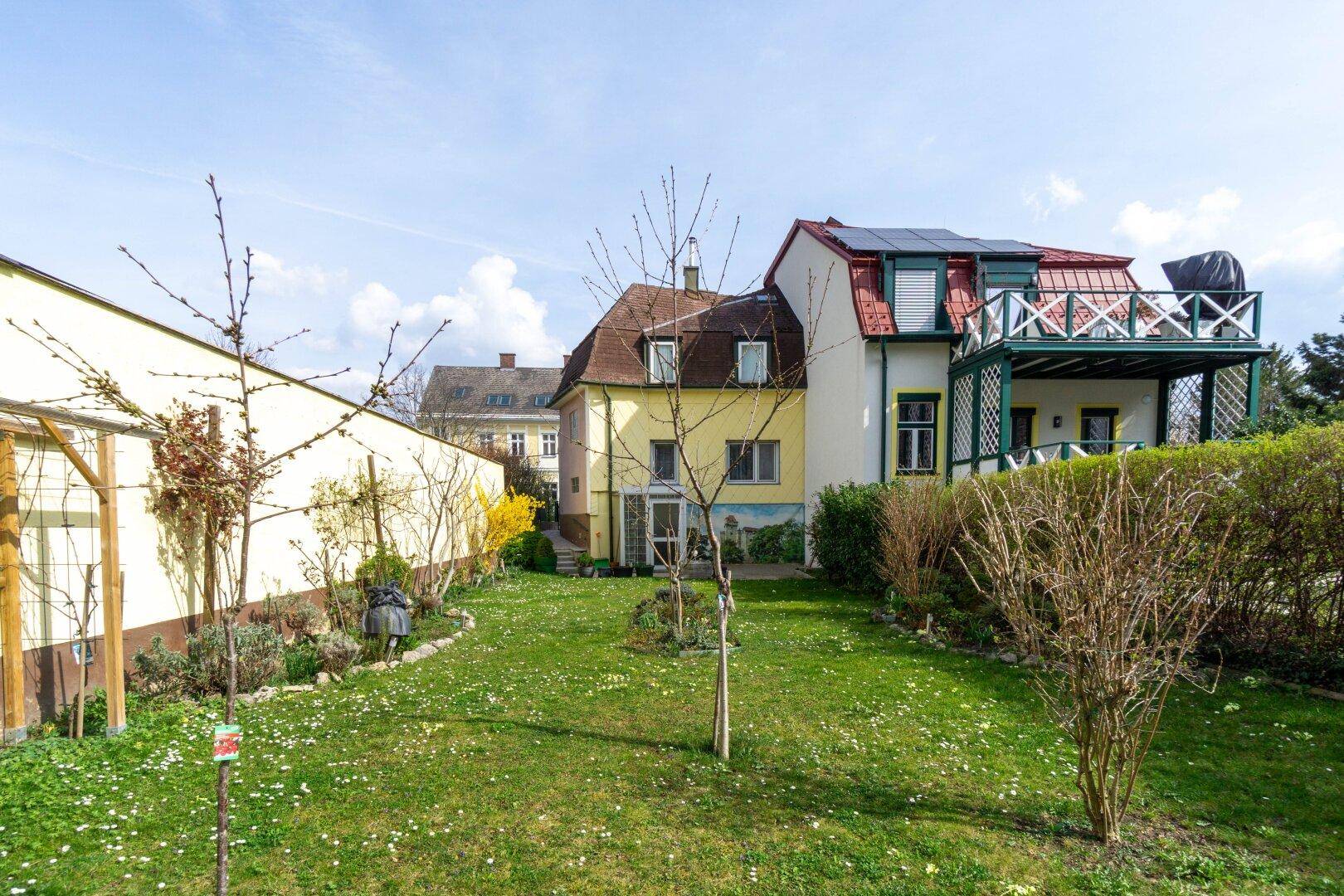 Weitläufiger Garten mit Blick auf die Rückseite des Hauses und einen Balkon mit Solaranlage.