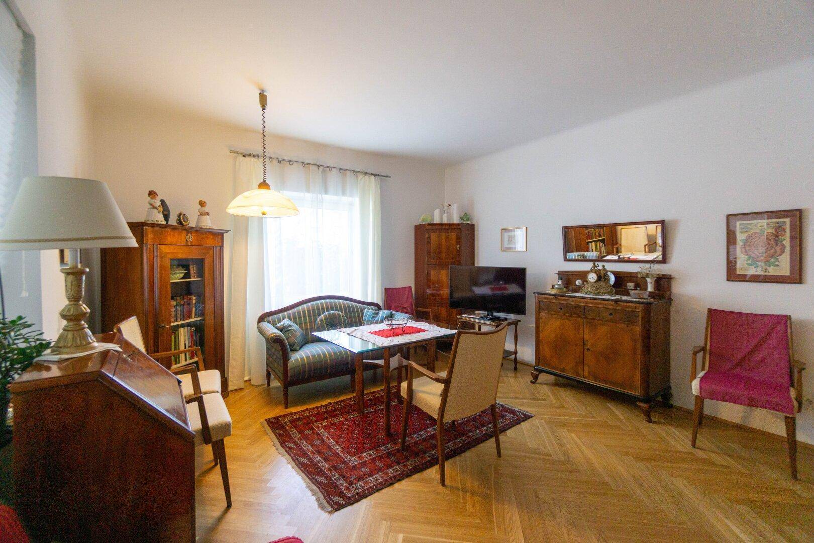 Gemütliches Wohnzimmer mit Fischgrätparkett, traditionellen Möbeln und einem Fenster.