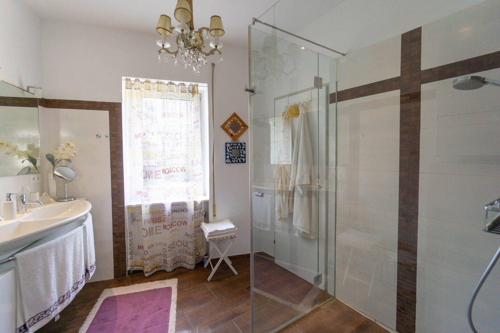 Helles Badezimmer mit moderner Glasdusche, Doppelwaschbecken und Fenster.