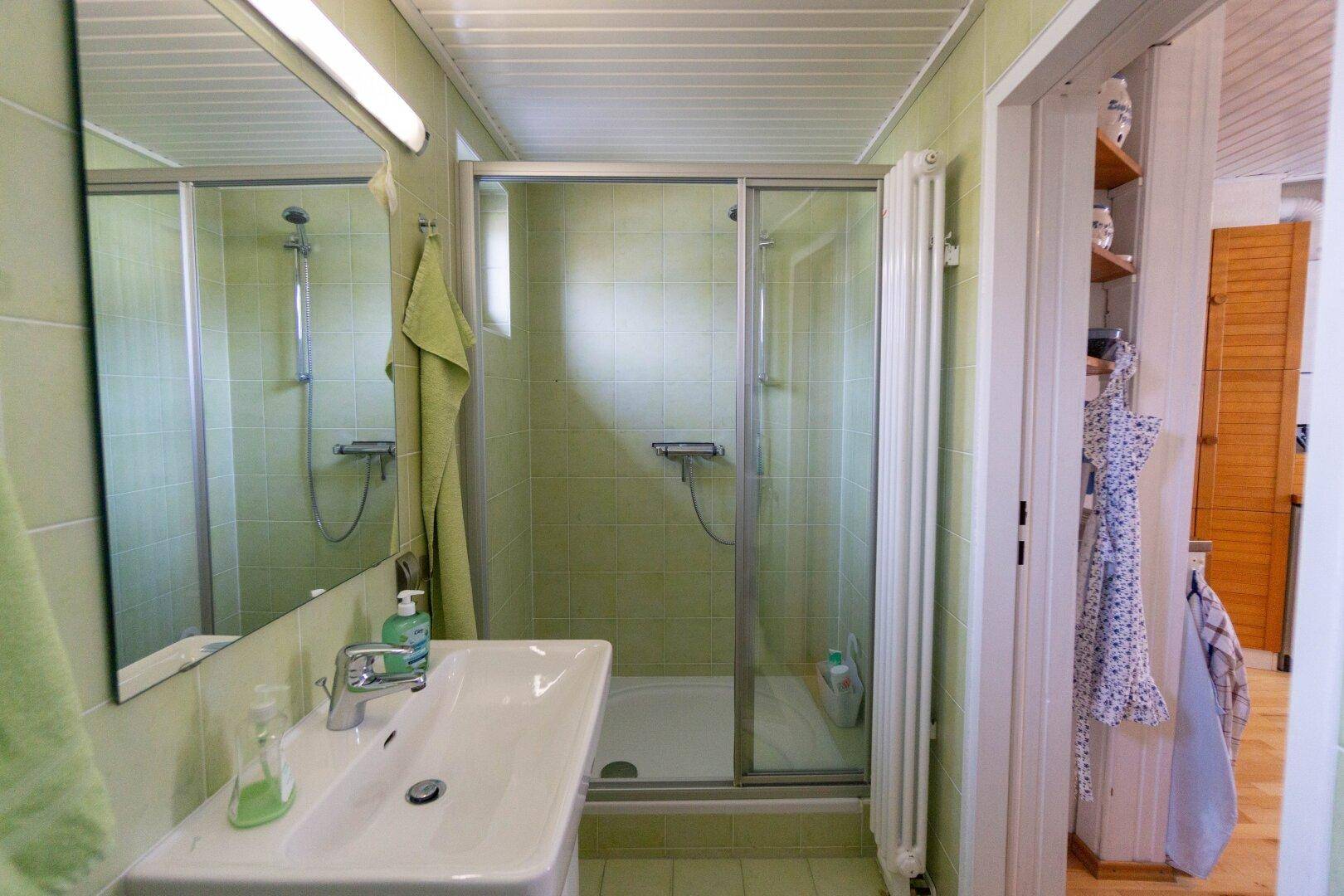 Funktionales Badezimmer mit grünen Fliesen und Duschkabine, ausgestattet mit einem Waschbecken.