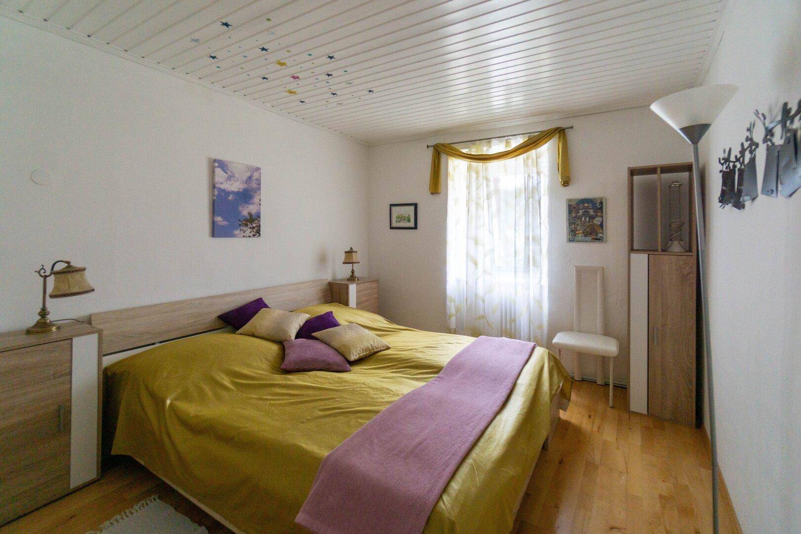 Schlafzimmer mit Holzboden, Doppelbett und Fenster, hell und freundlich eingerichtet.