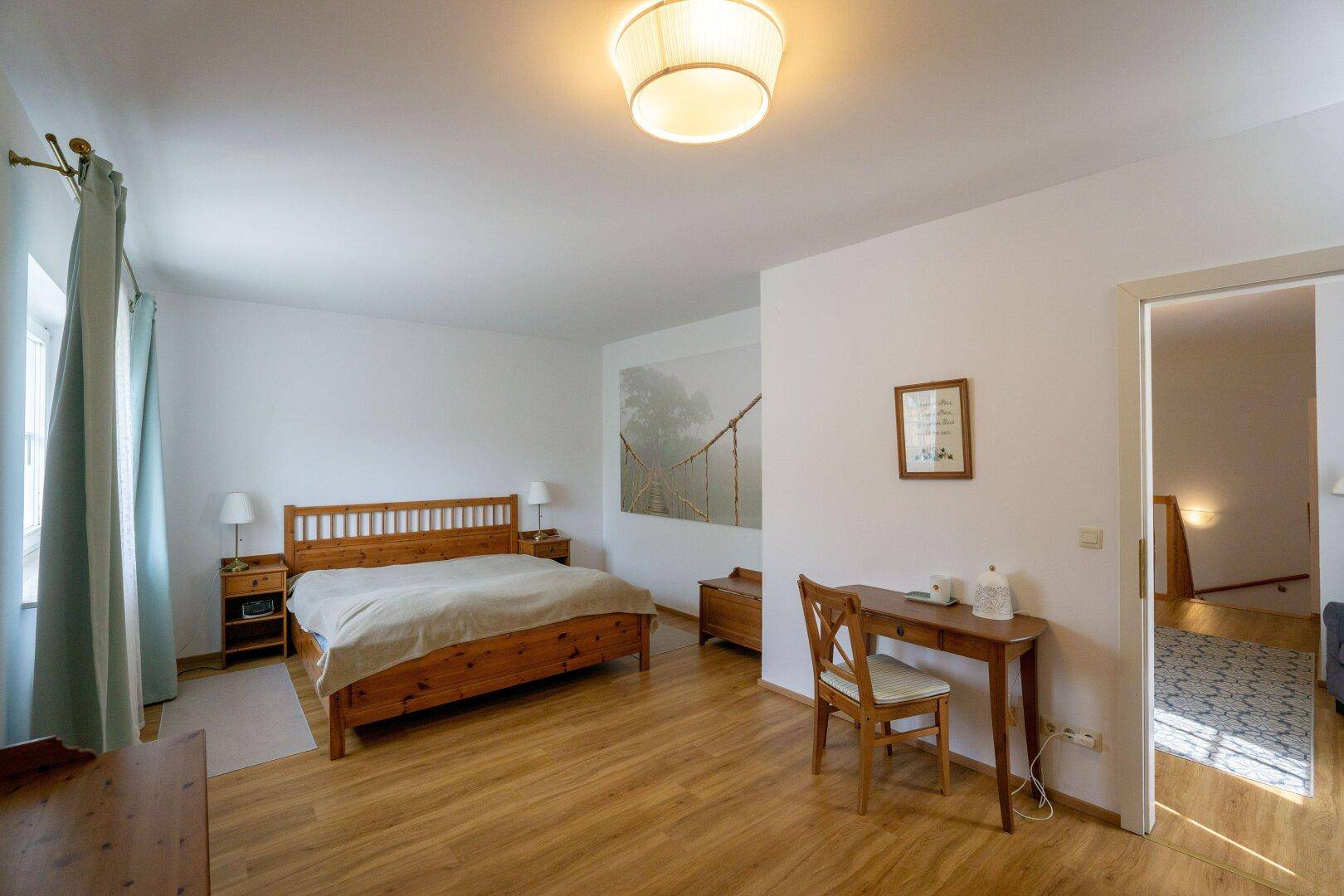 Geräumiges Schlafzimmer mit Holzbett, Schreibtisch und hellem Holzboden.
