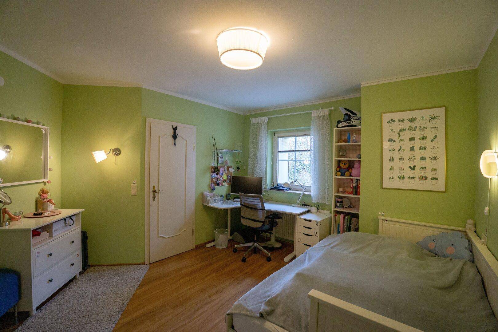 Kinderzimmer mit grün gestrichenen Wänden, Schreibtisch und Holzboden.