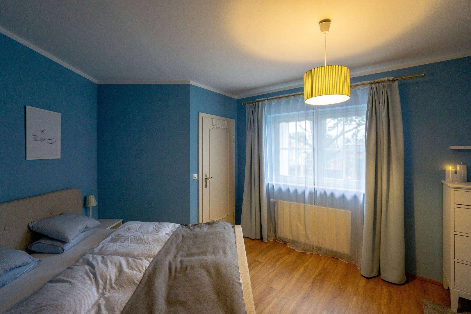 Schlafzimmer mit blauen Wänden, Holzboden und einem großen Fenster.