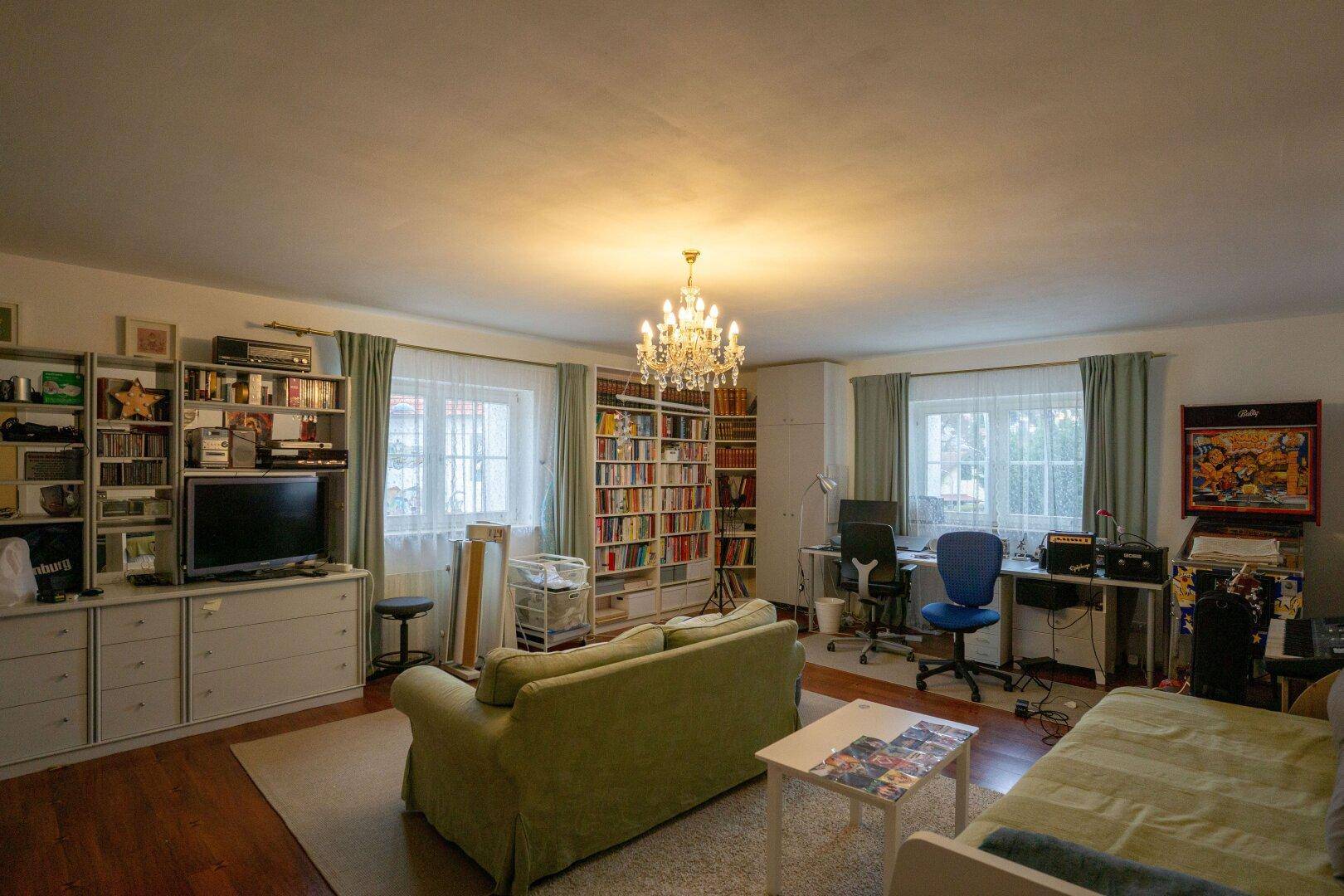 Geräumiges Wohnzimmer mit Bücherregalen, Sofa und einem Arbeitsbereich.