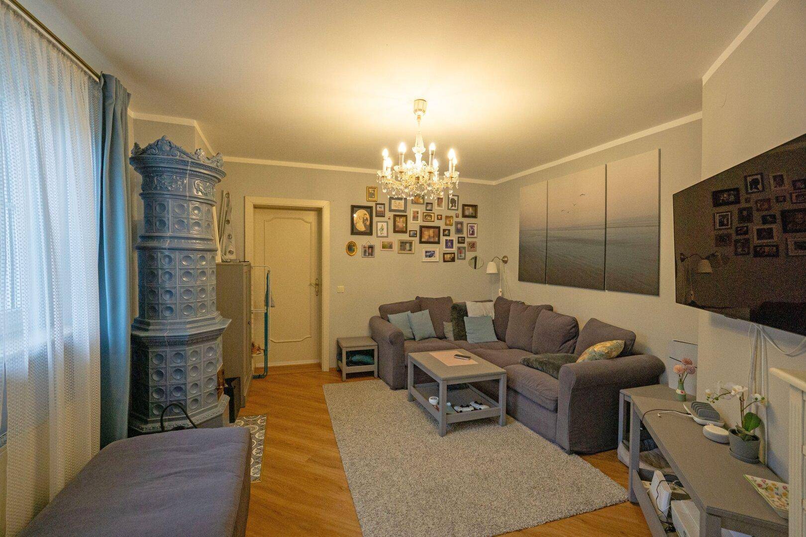 Gemütliches Wohnzimmer mit blauem Kachelofen, Ecksofa und vielen Bildern an der Wand.