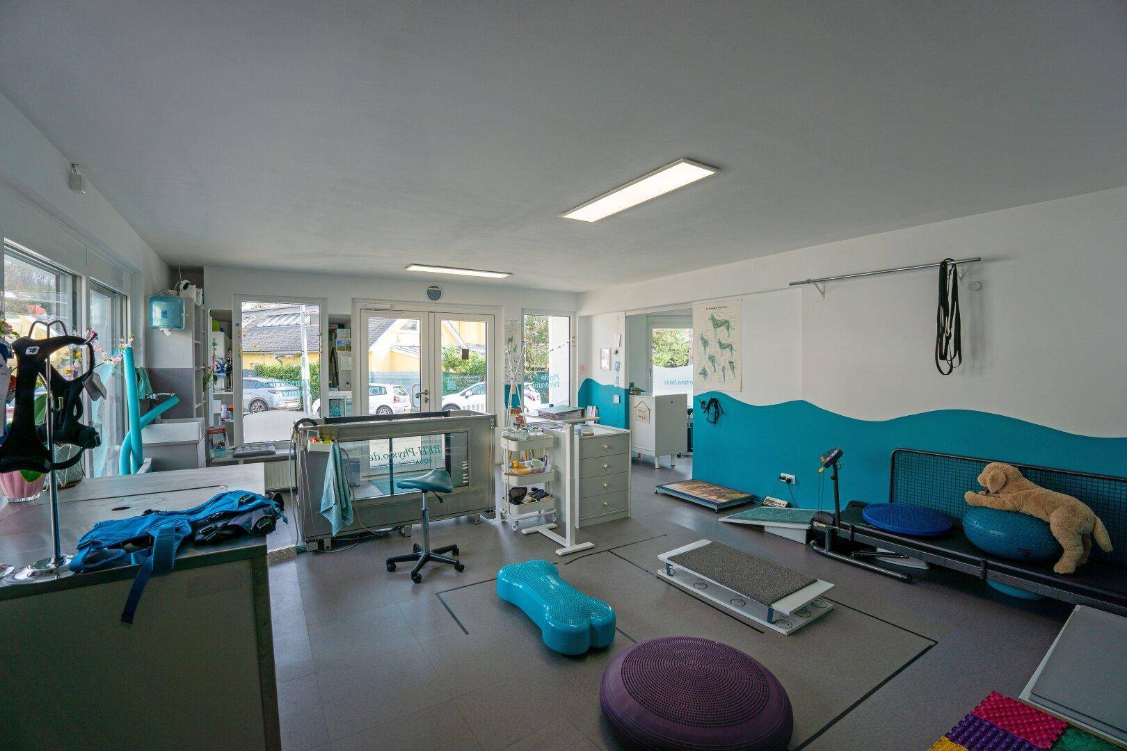 Helles Geschäftslokal mit großen Fenstern und Ausstattung für Physiotherapie.