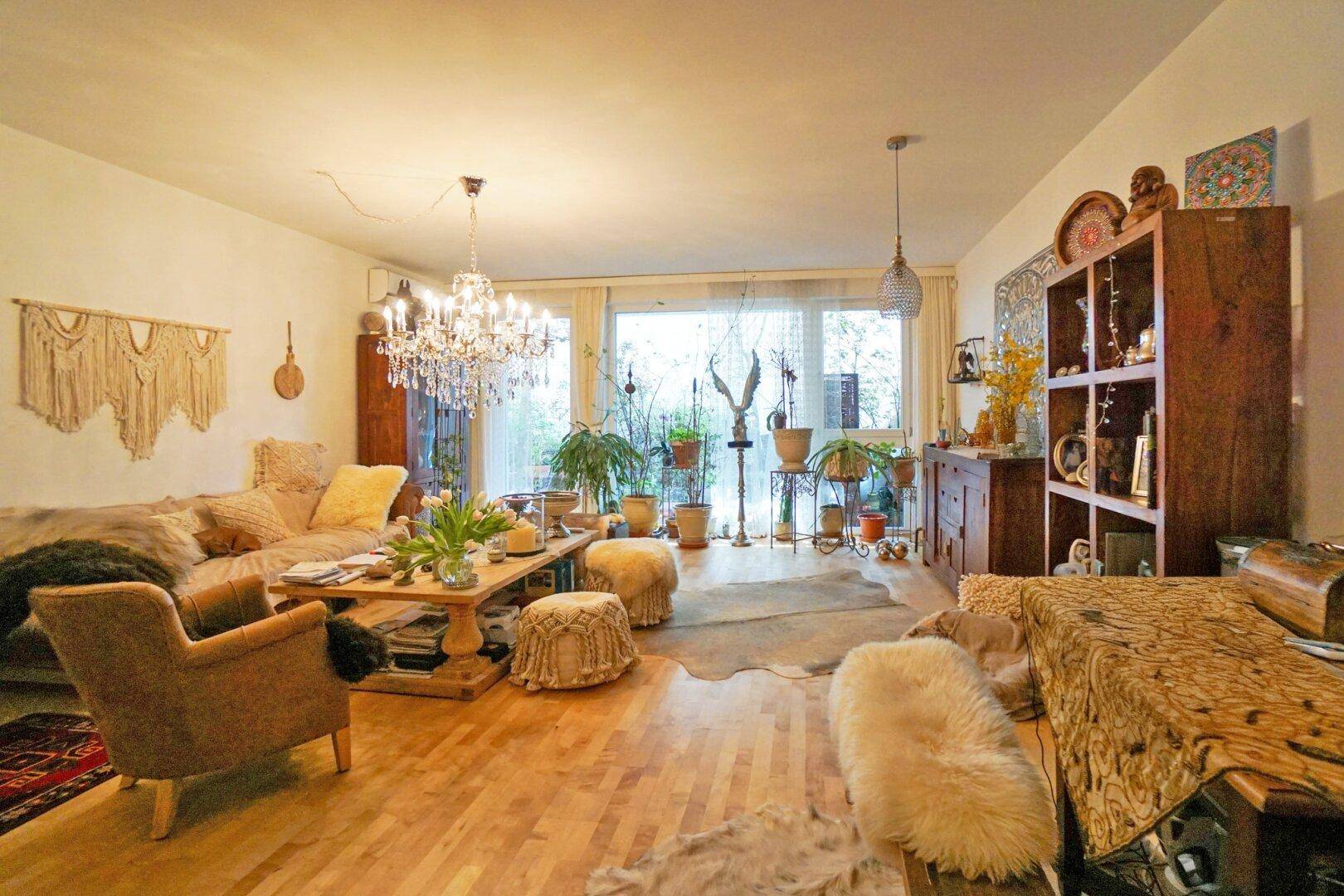 Geräumiges Wohnzimmer mit Holzboden, Kronleuchter und vielen Pflanzen, das zum Entspannen einlädt.