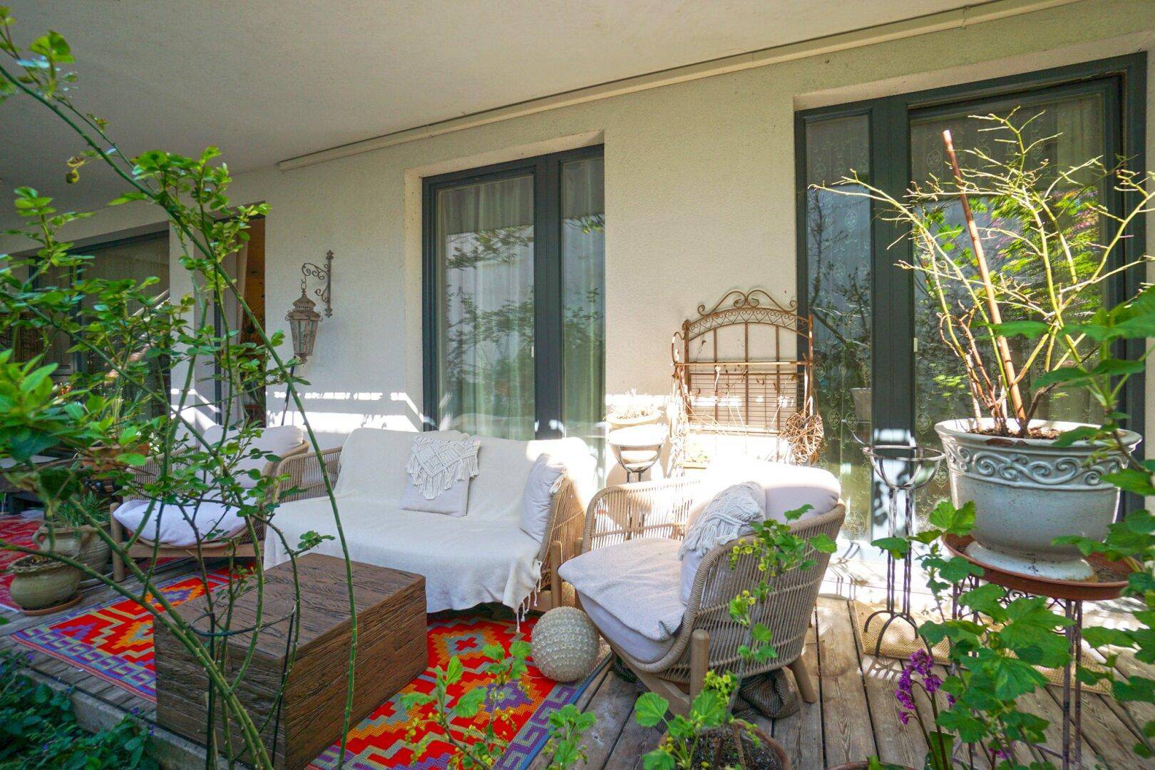 Sonnige Terrasse mit bequemen Gartenmöbeln und vielen Topfpflanzen, ideal zum Entspannen.